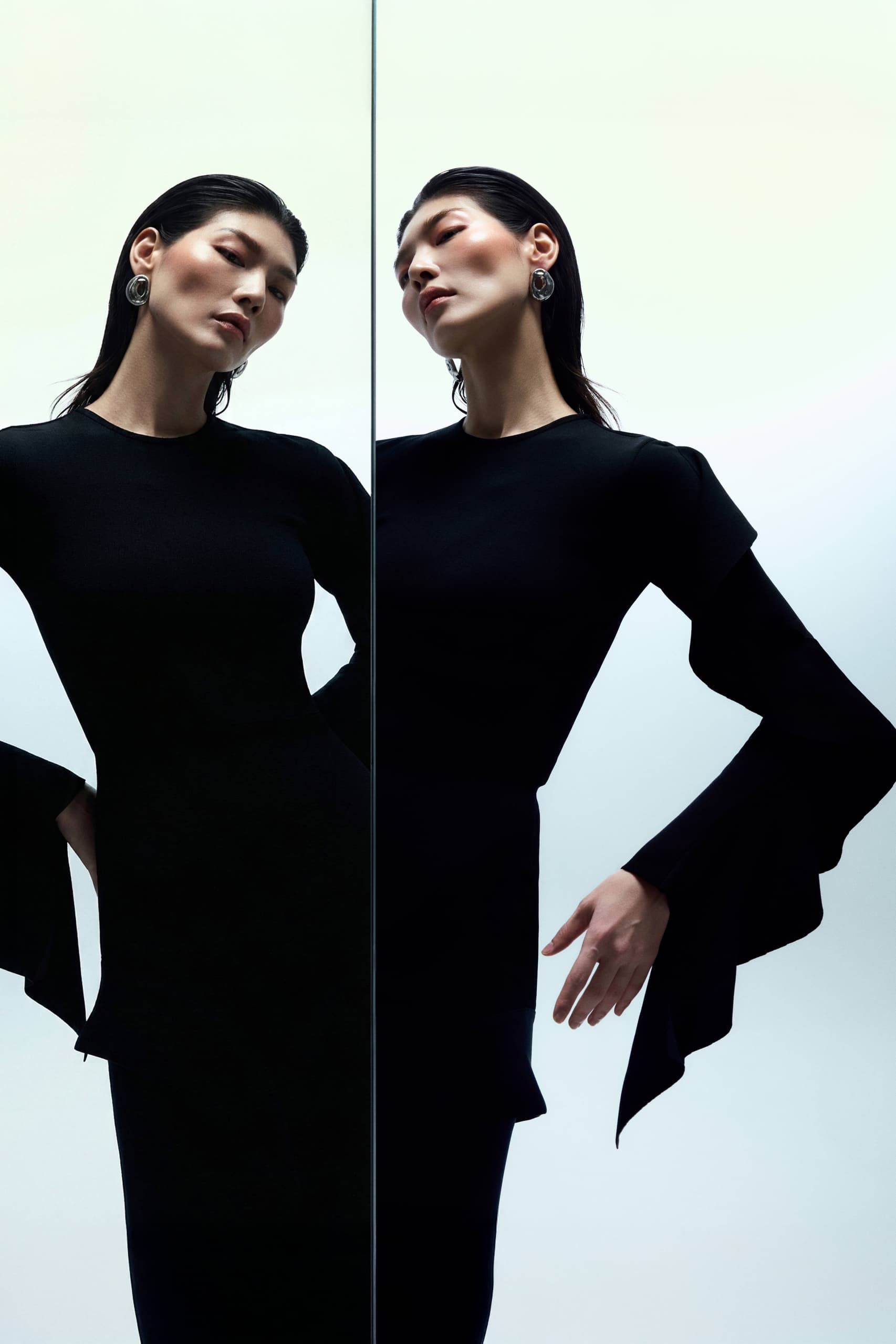 Elegant woman in black dress mirrored reflection, stylish pose.
