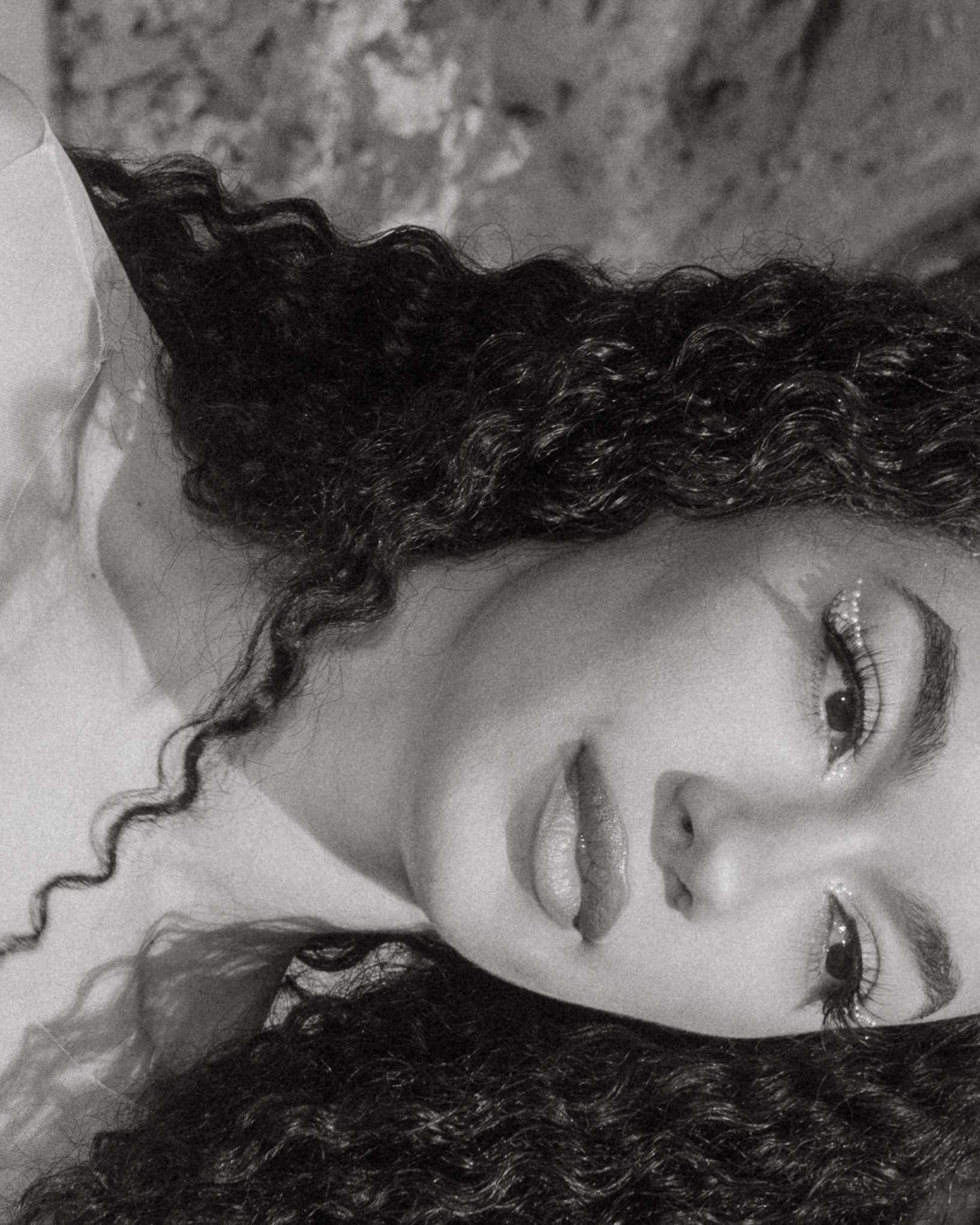Black and white portrait of a woman with curly hair looking peaceful.