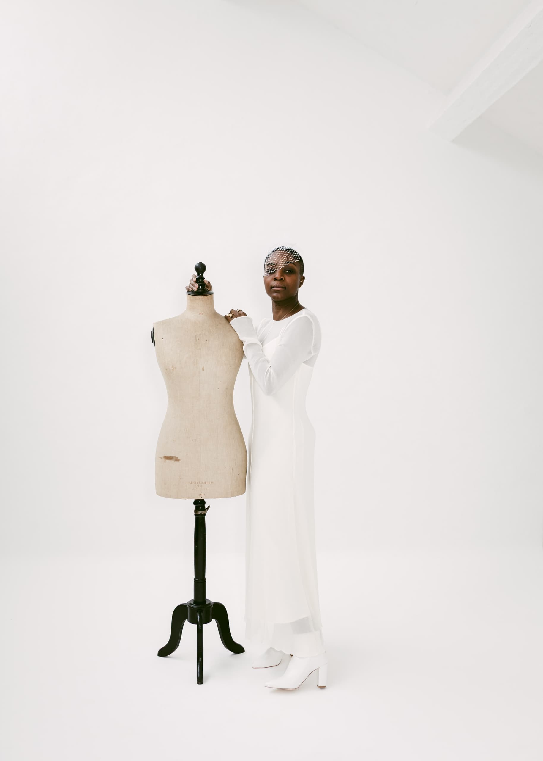 Fashion designer in white dress with mannequin in minimalist studio setting.