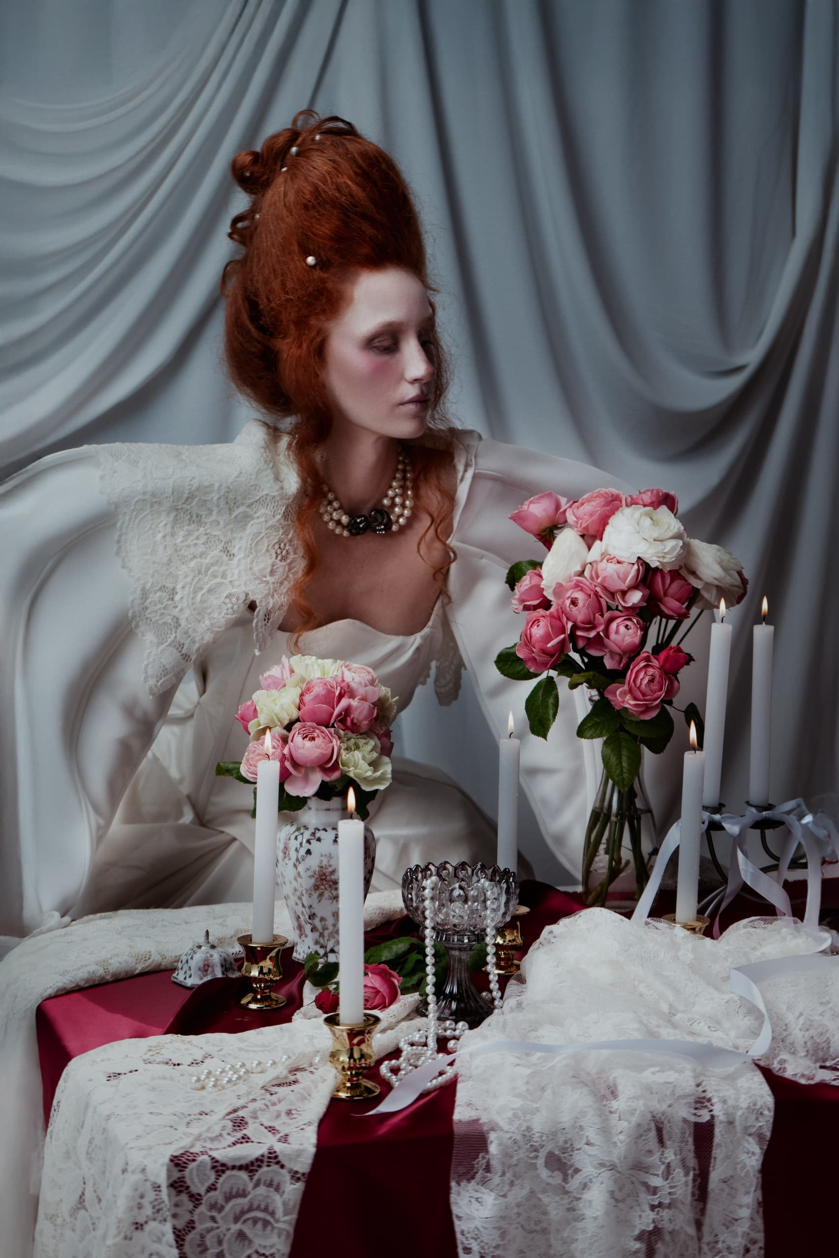 Elegant woman in vintage dress with flowers and candles in romantic setting.