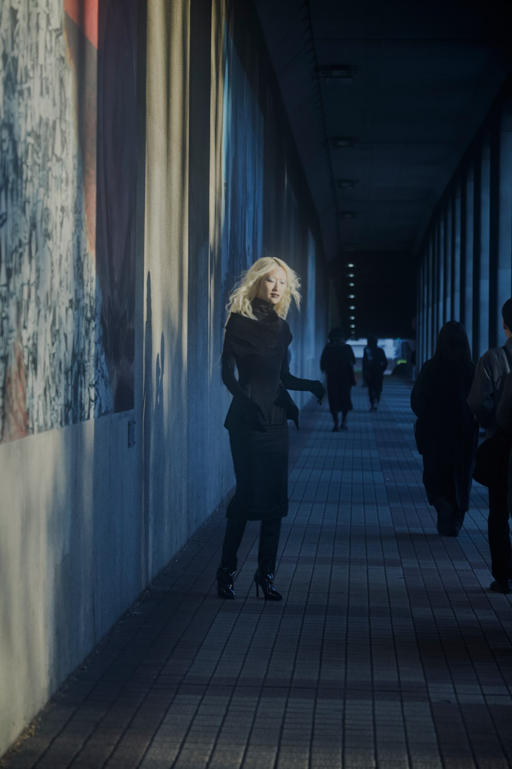 Woman in black coat walking through a dimly lit urban passageway.