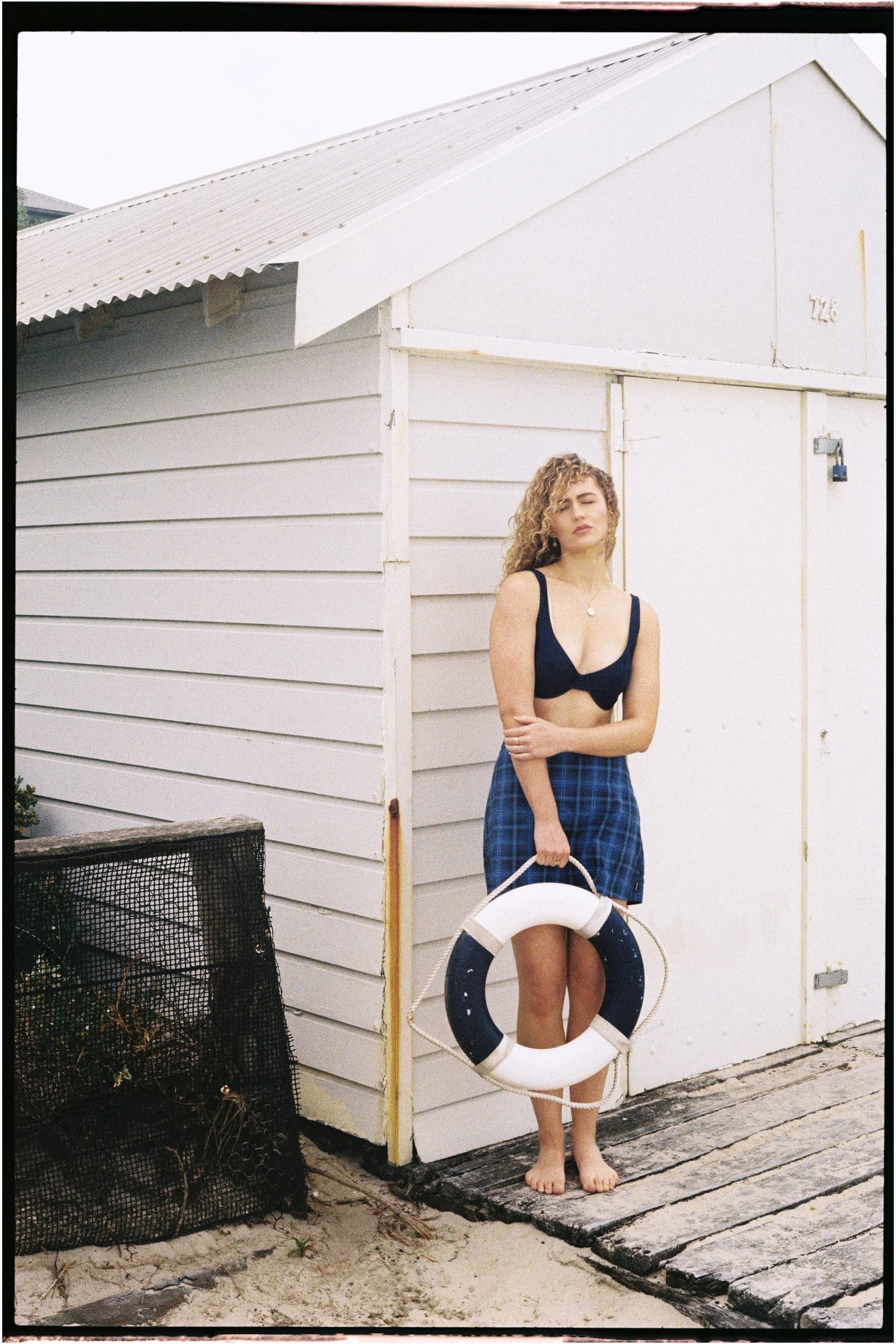Woman in swimwear holding lifebuoy by beach hut.