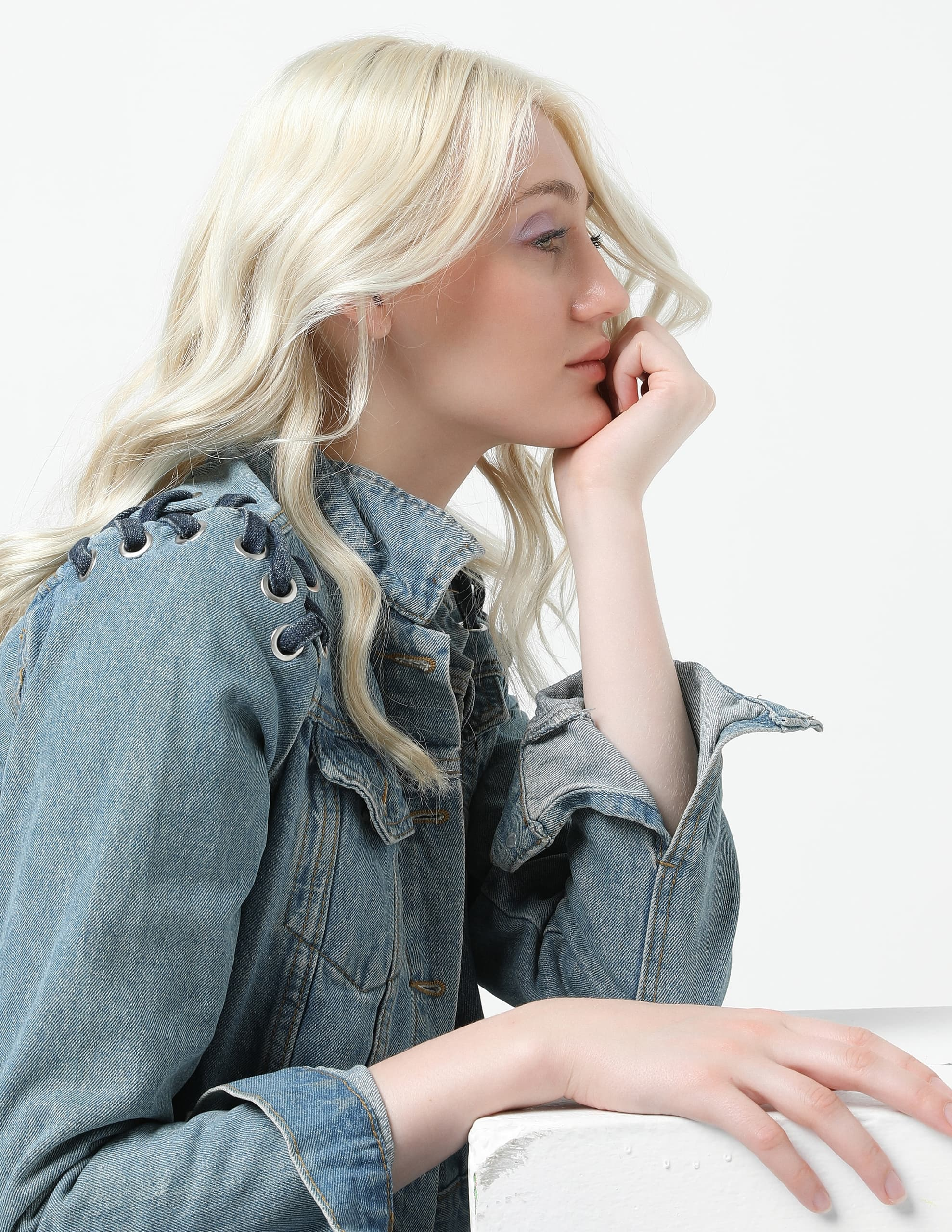 Blonde woman in a denim jacket looking contemplative against a white background.
