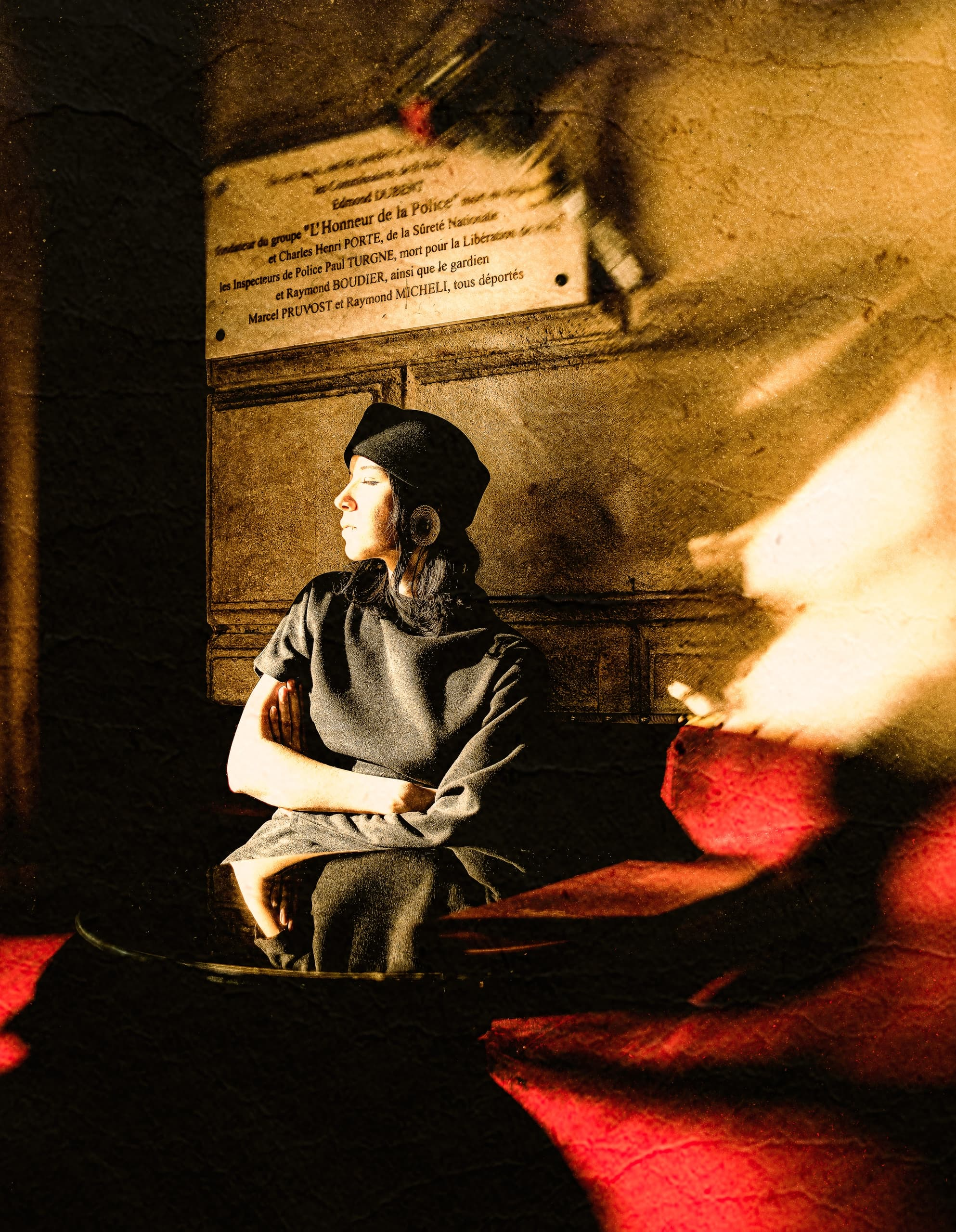 Vintage scene: woman in beret sitting under warm light with plaque background.