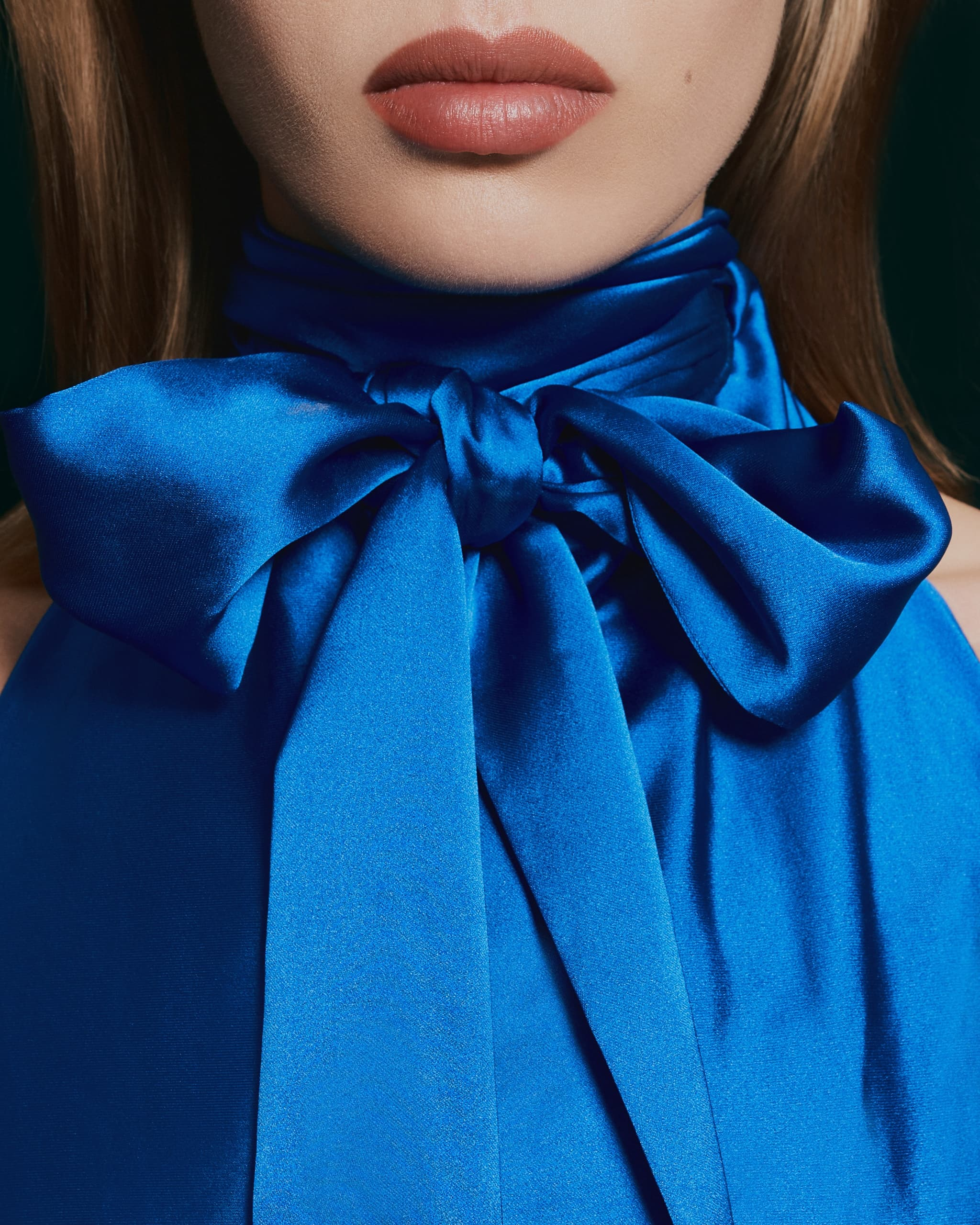 Blue silk bow tie top, close-up on neck and lipstick-wearing lips.