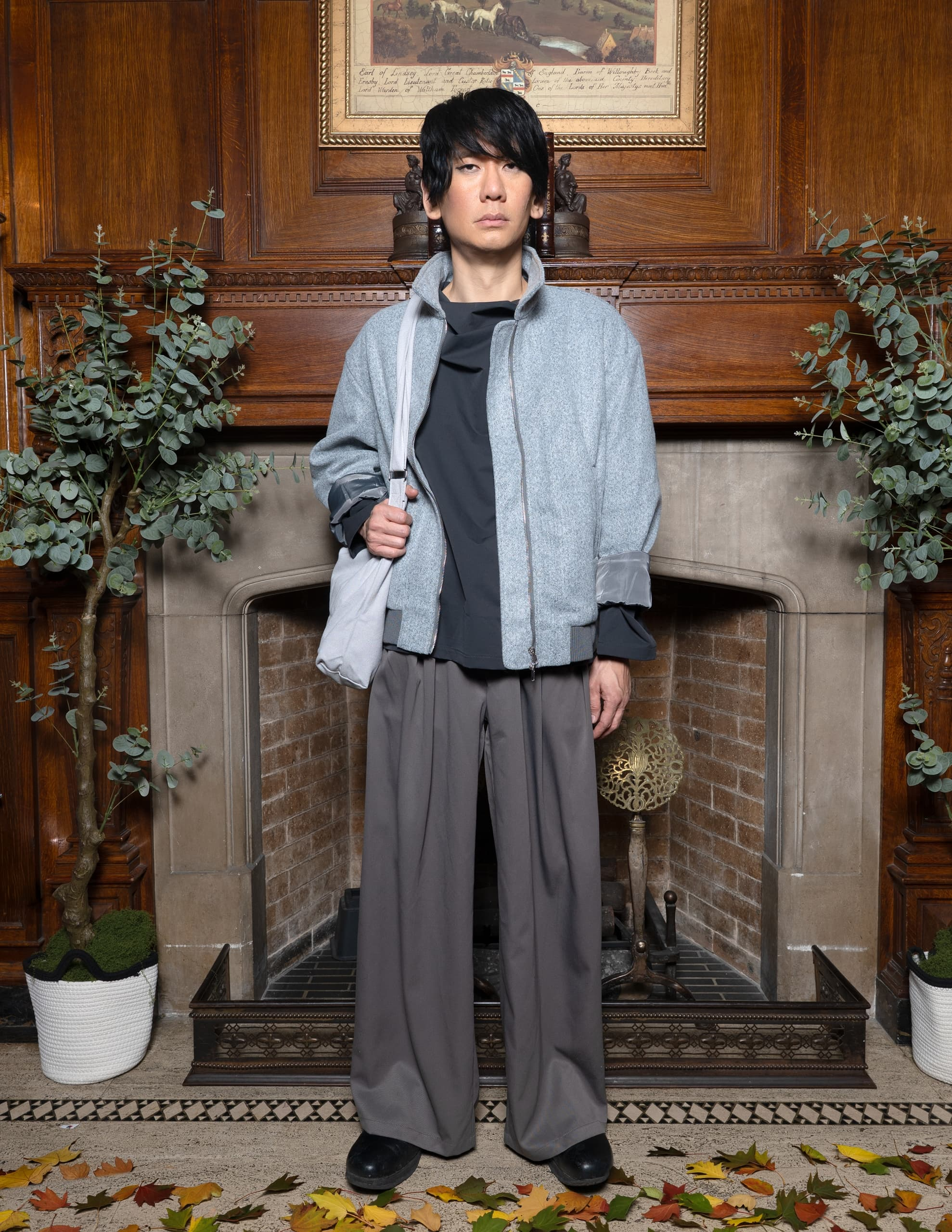 Person in stylish outfit standing by a fireplace with autumn leaves on the floor.