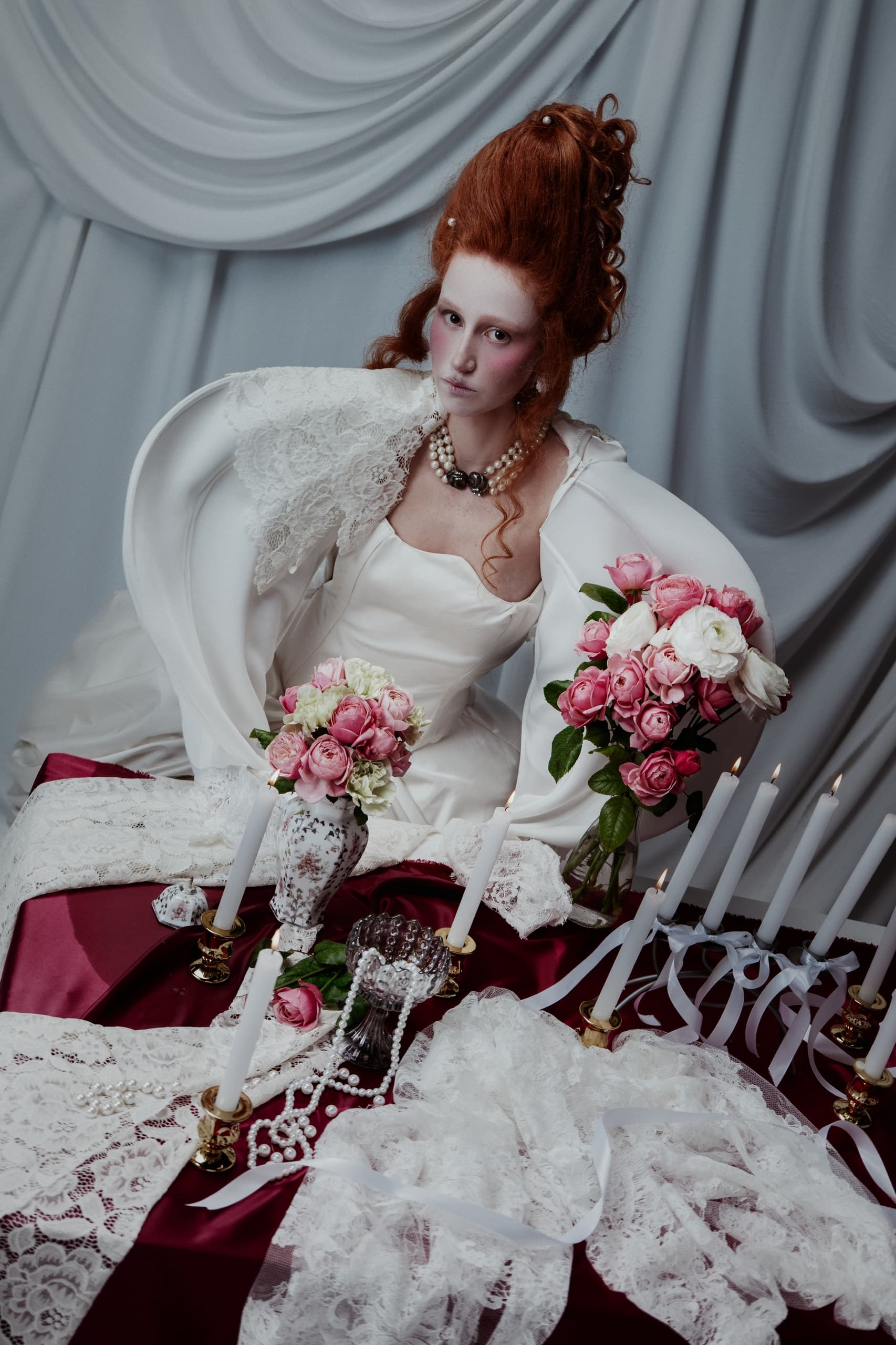 Elegant woman in vintage dress with roses and candles on a decorative table.