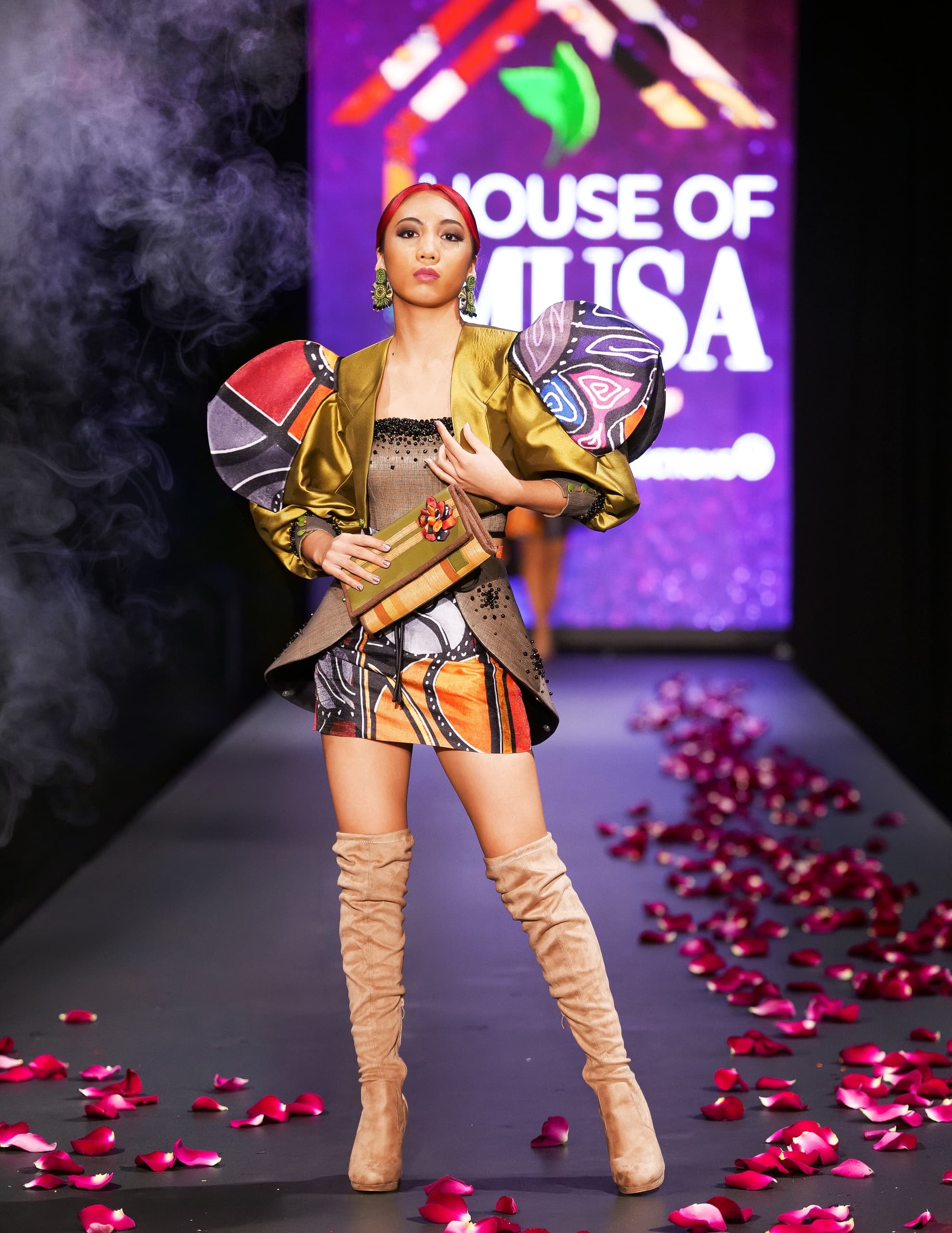 Model walks runway in colorful dress with dramatic sleeves at a fashion show.