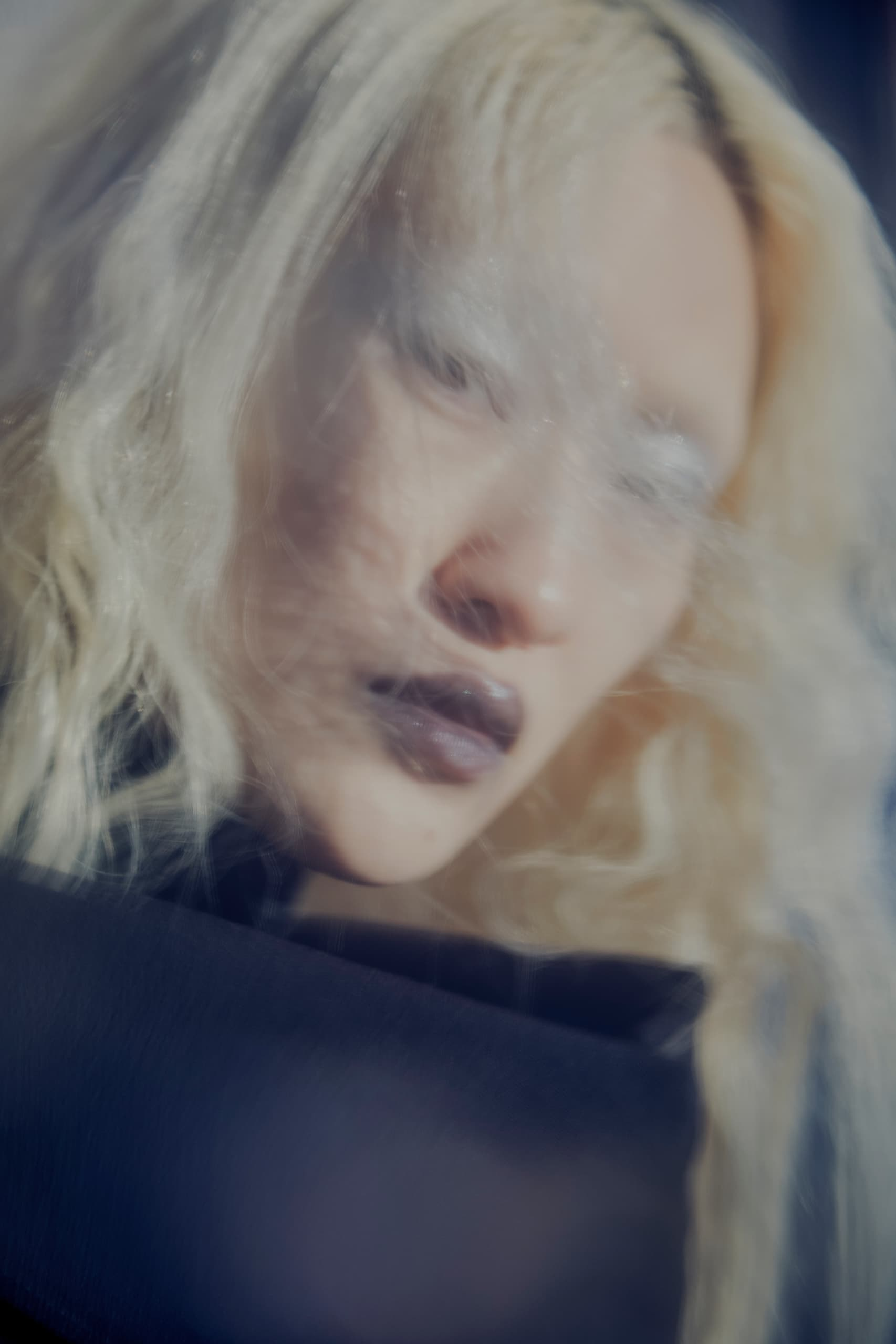 Blurry ethereal portrait of a person with blonde hair wearing a dark outfit.