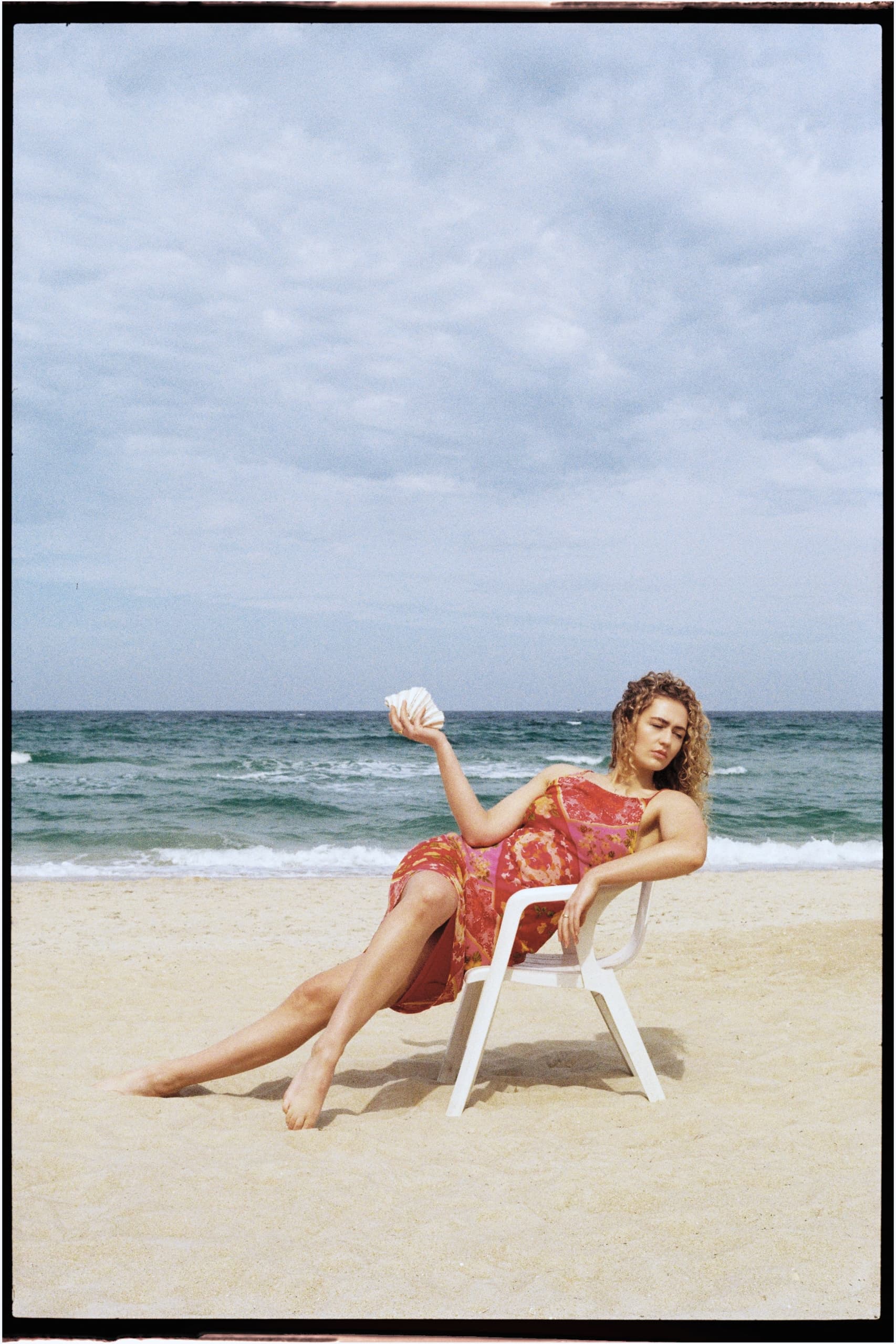 Woman in a beach chair holding seashells, relaxing by the ocean.