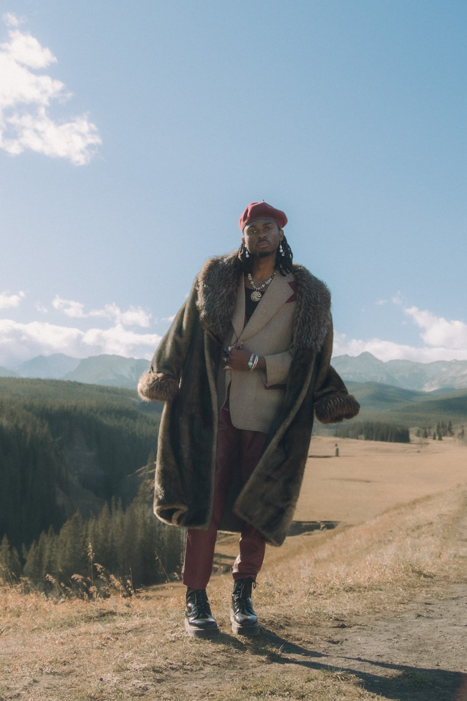 Stylish man in fur coat and beret in scenic mountain landscape.