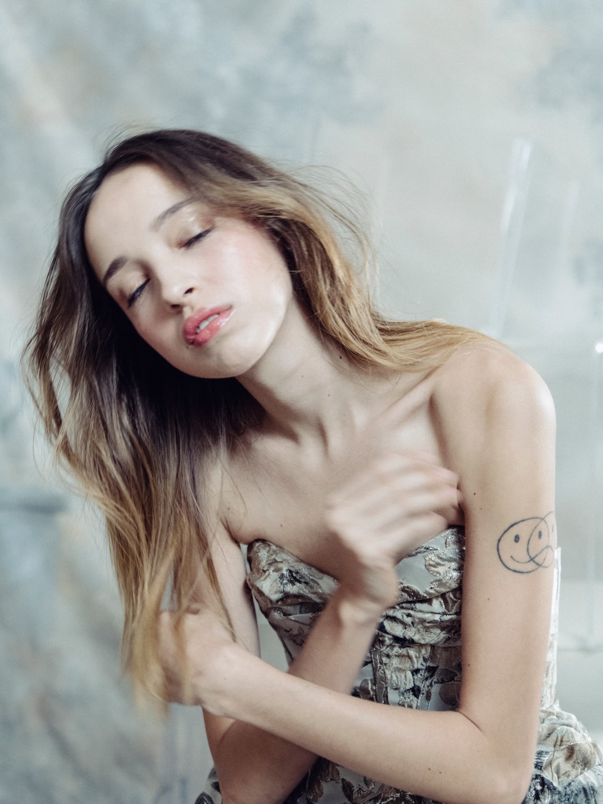 Woman in floral dress with tattoo, eyes closed, lost in thought.