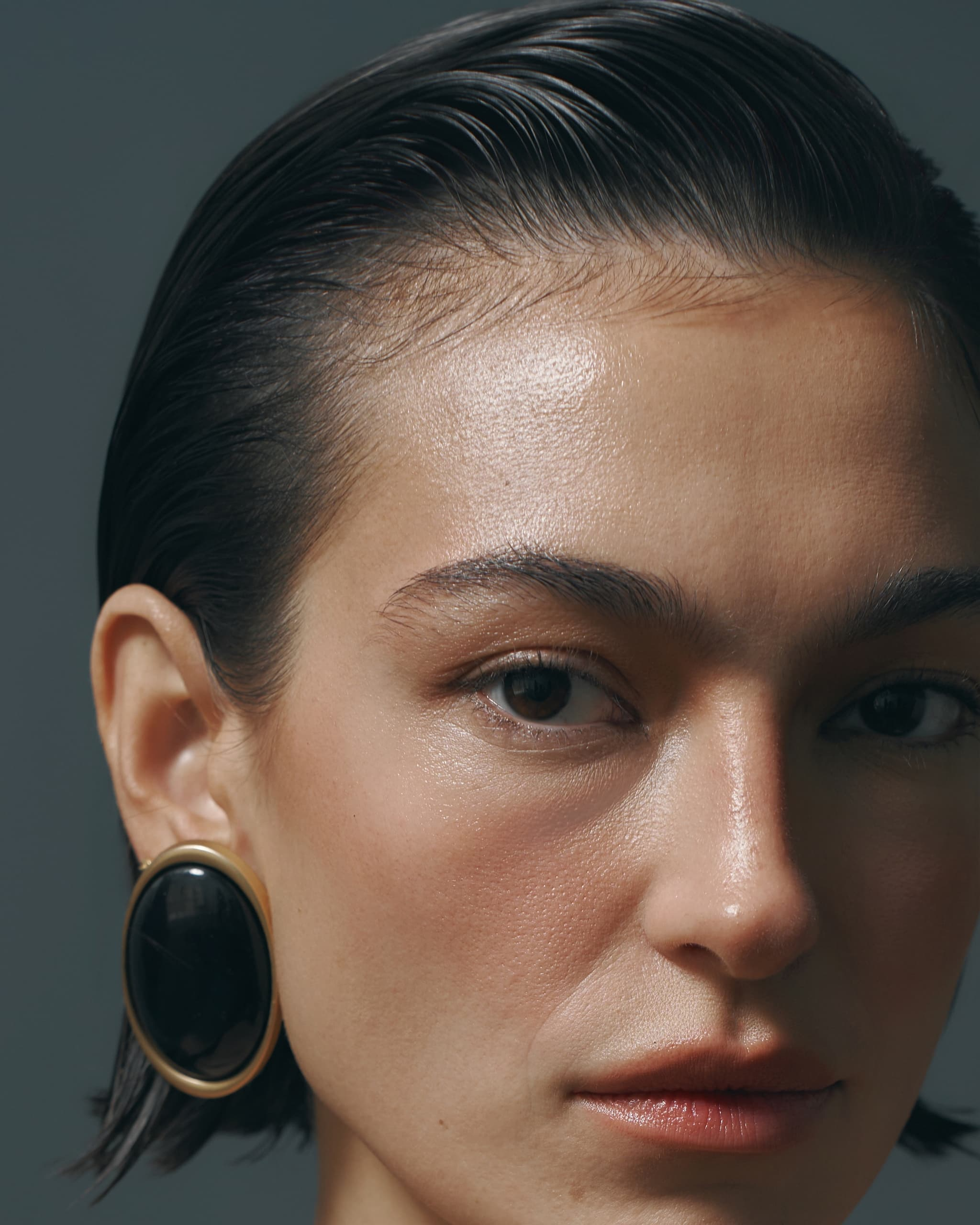 Close-up of a woman with slicked-back hair and large black earrings.