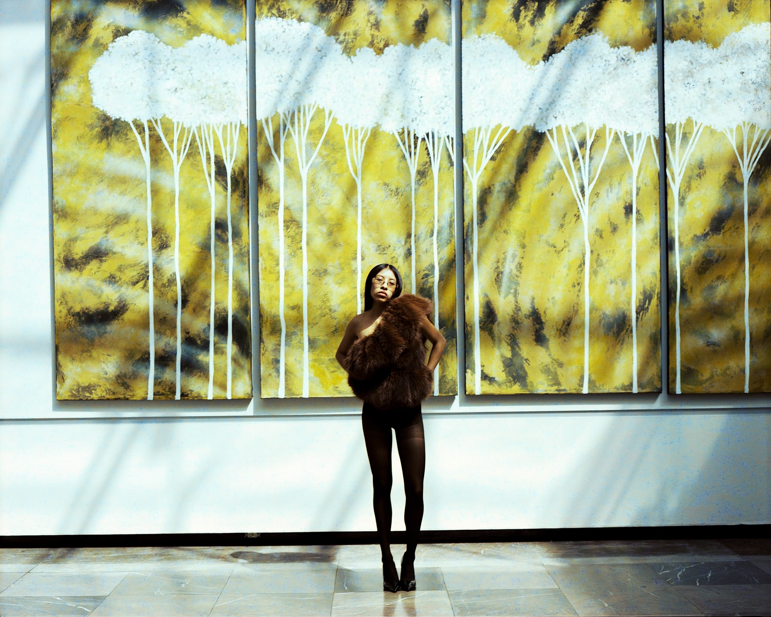 Person posing in front of large abstract tree artwork on a sunny day.