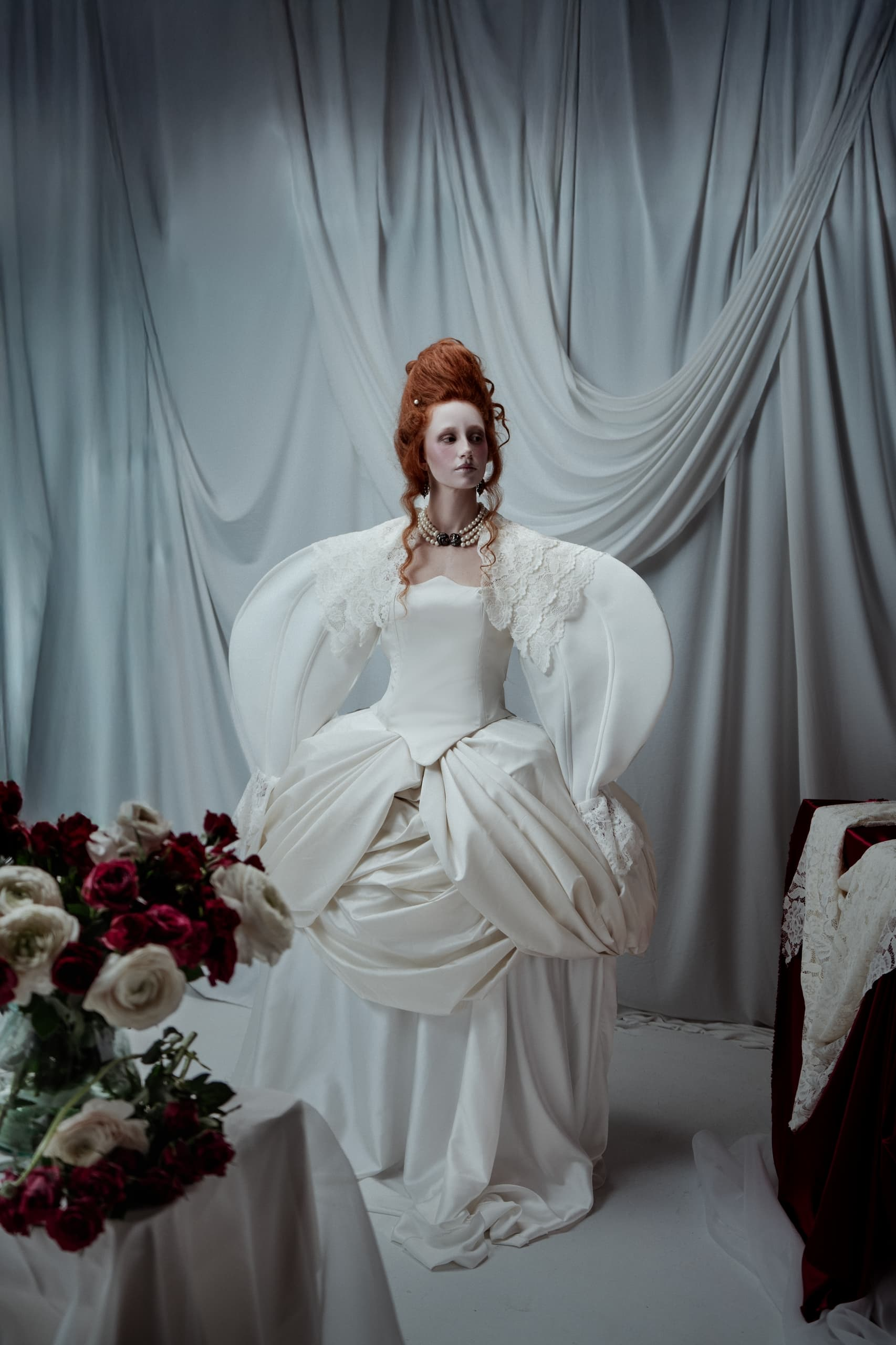 Elegant woman in Victorian-inspired gown with red hair and floral arrangements.