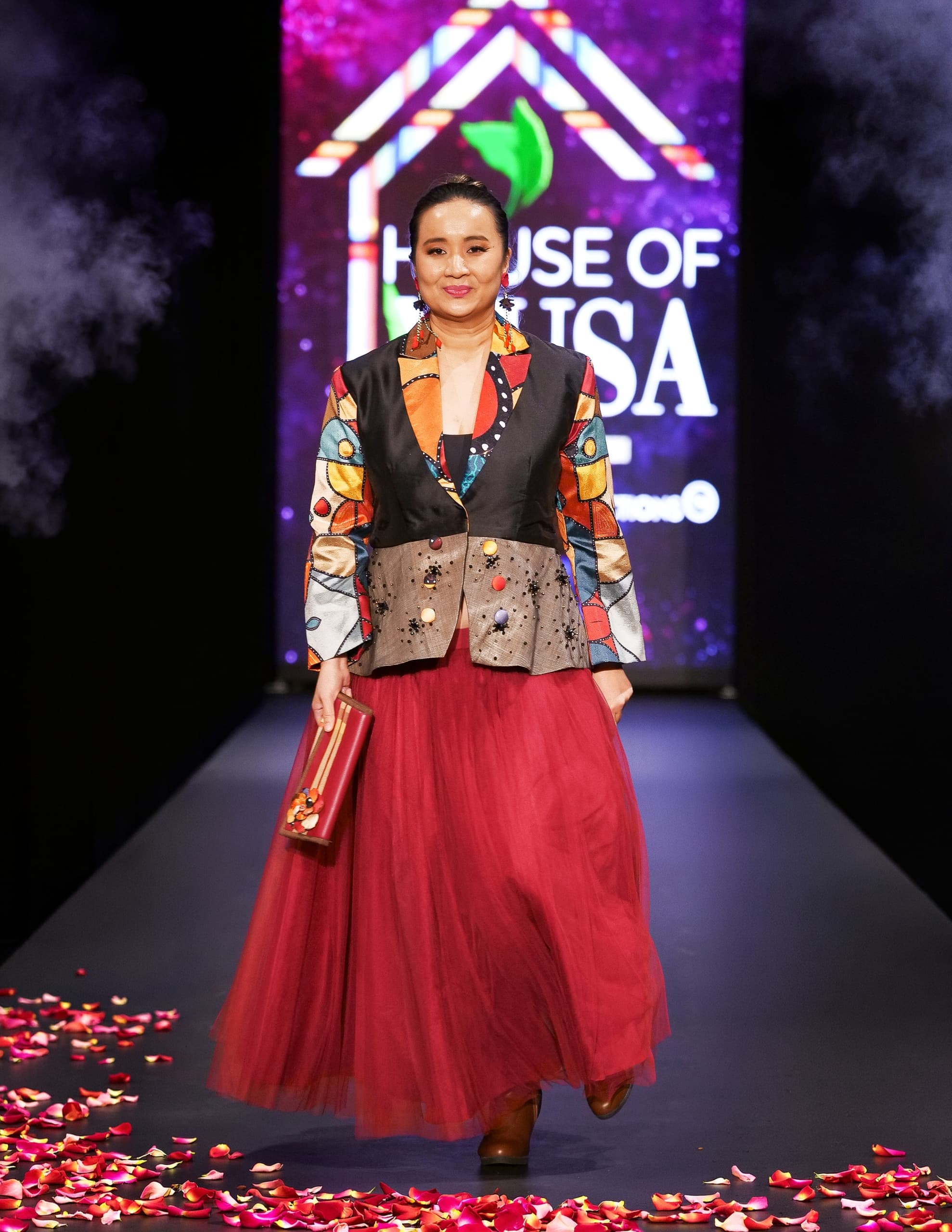 Model in vibrant outfit walking a floral runway at fashion event.
