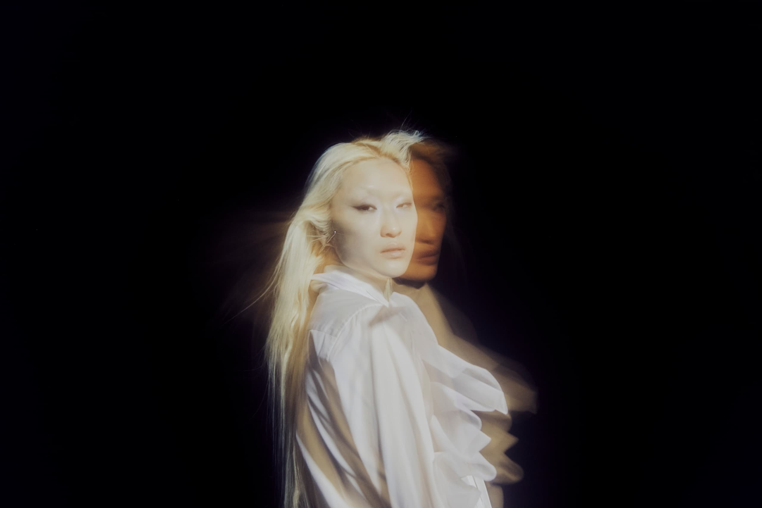 Artistic portrait with motion blur effect and ethereal lighting on a black background.