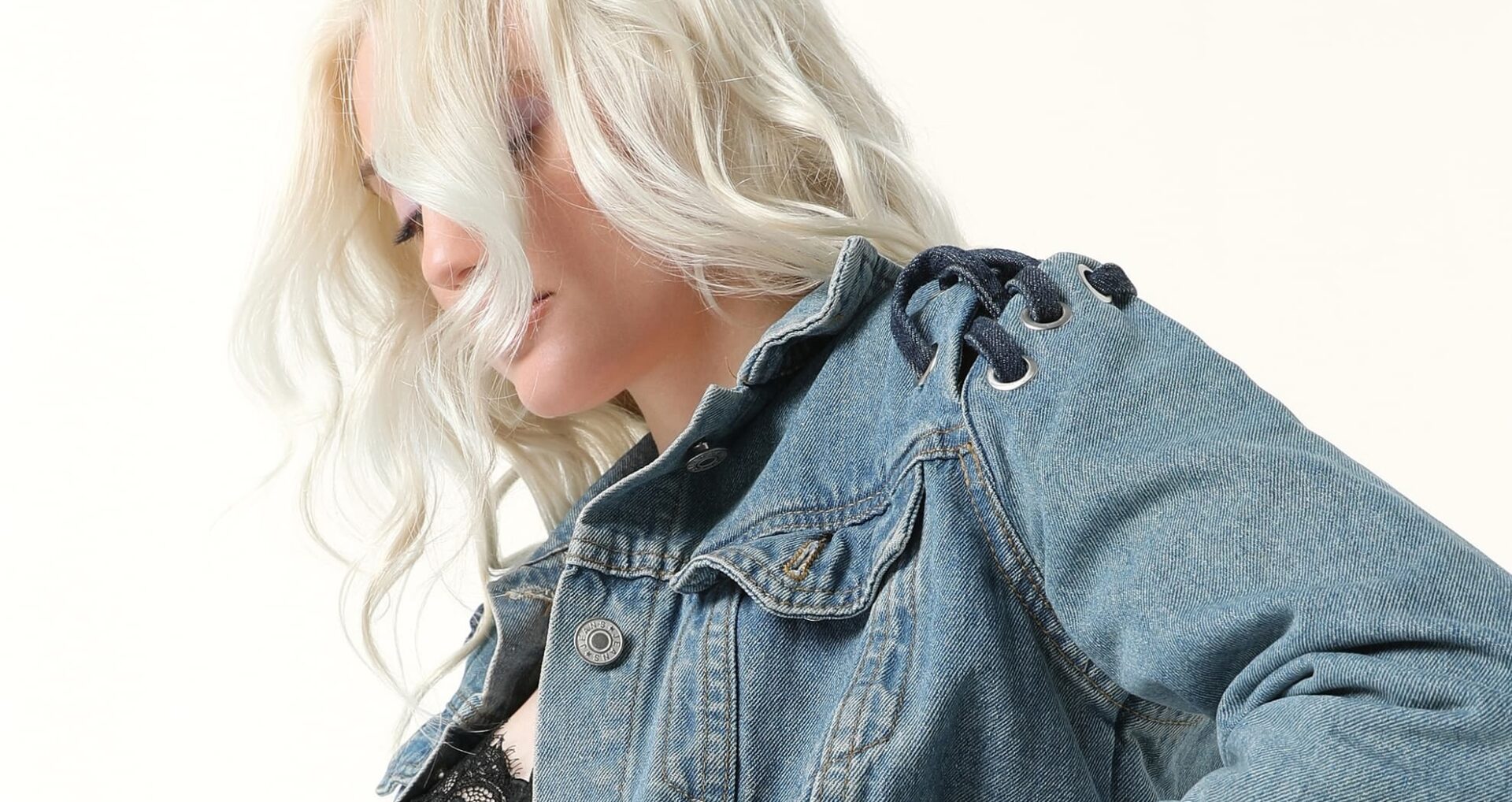 Woman in denim jacket with lace detail and wavy blonde hair.