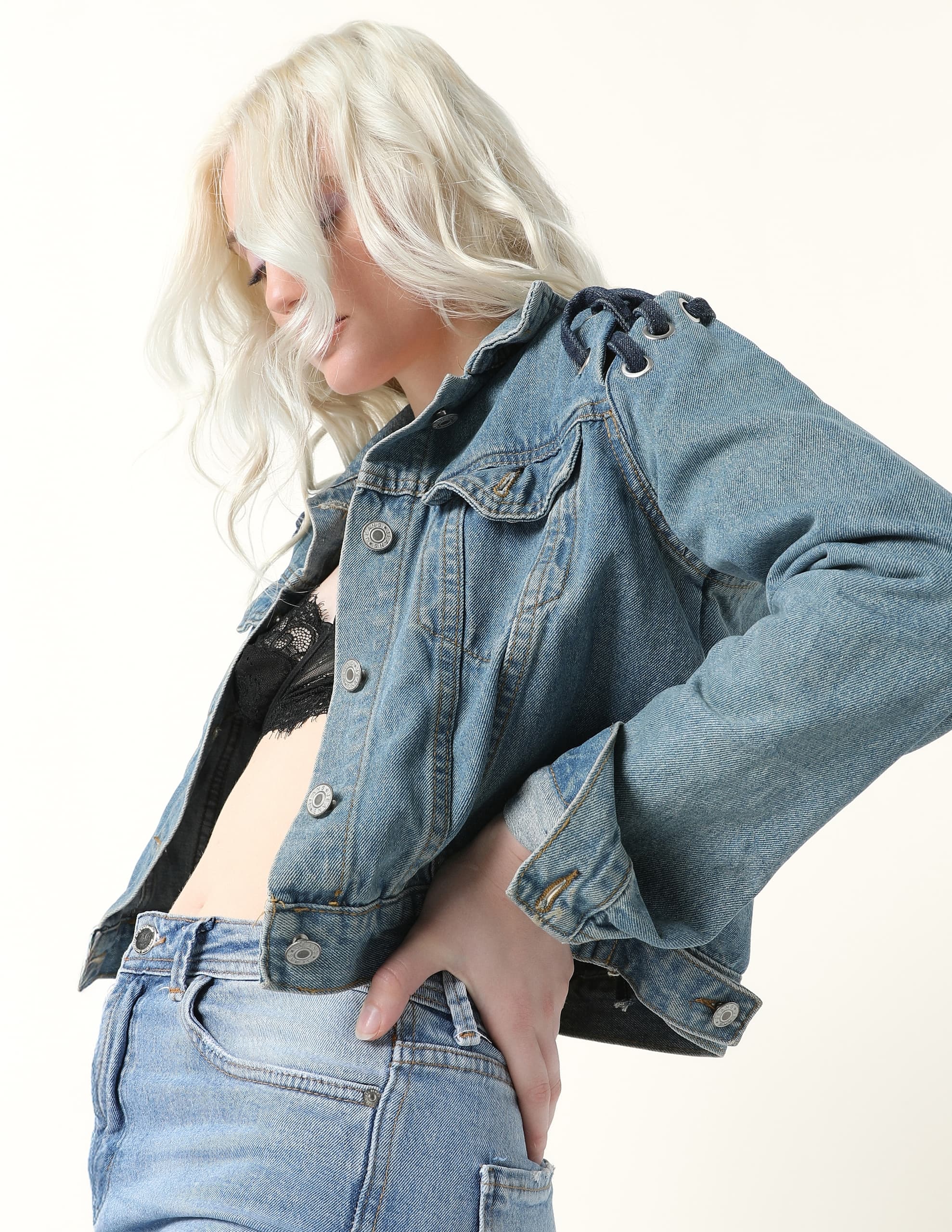 Woman in denim jacket and jeans with blonde hair against a white background.