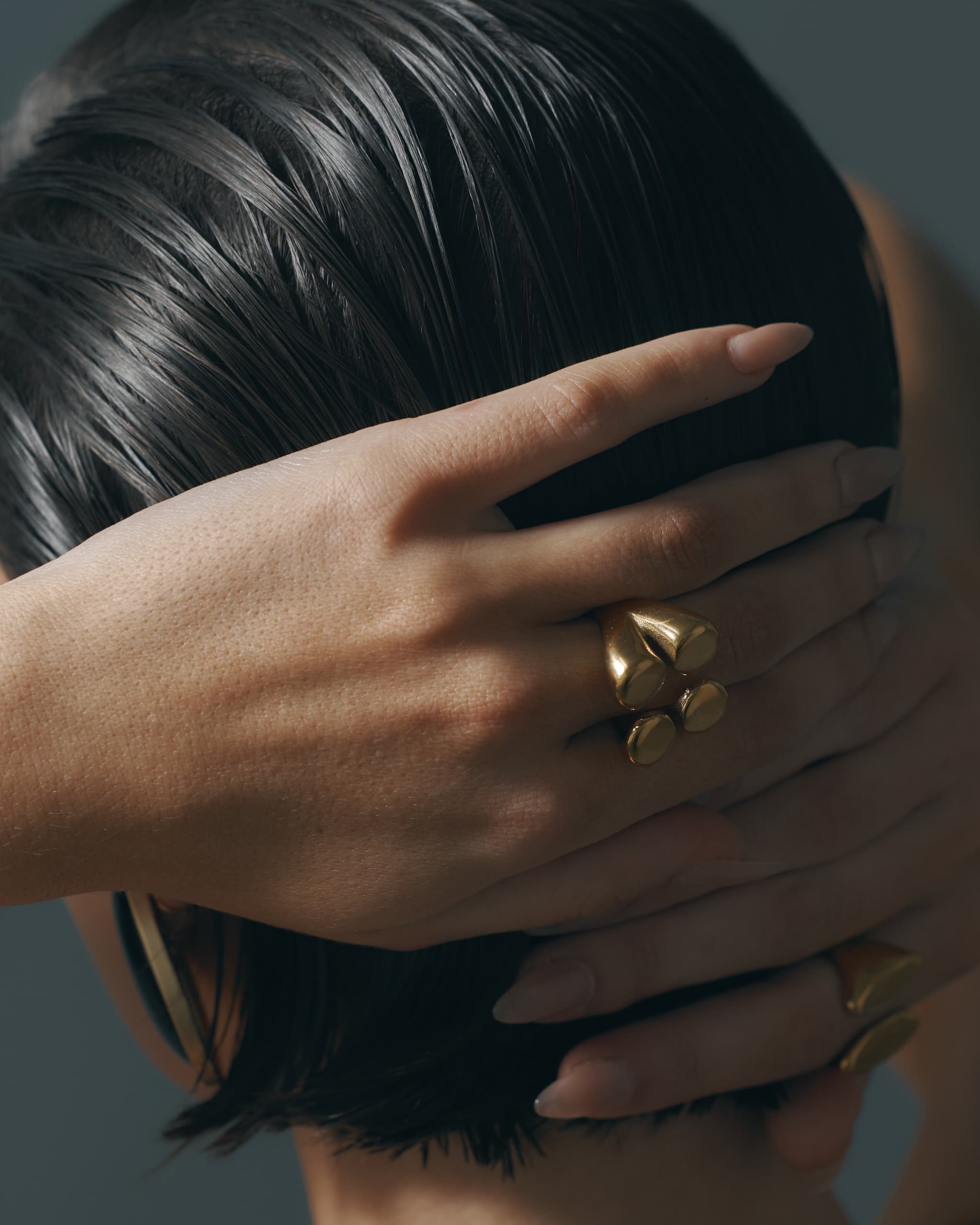 Woman's hands with gold rings, holding short wet hair stylishly.