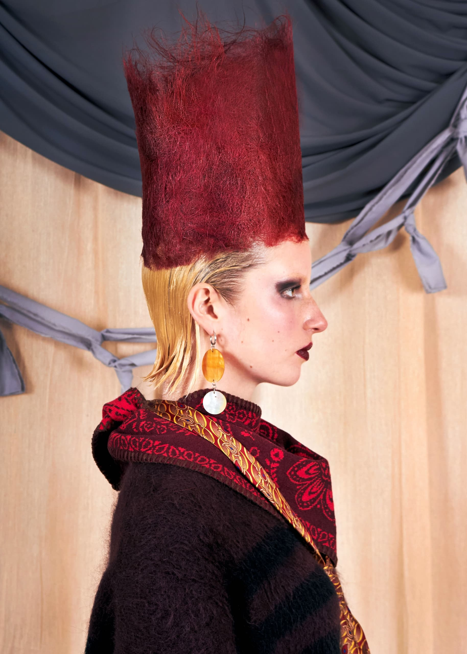 Avant-garde fashion model with tall red hair and vibrant accessories.