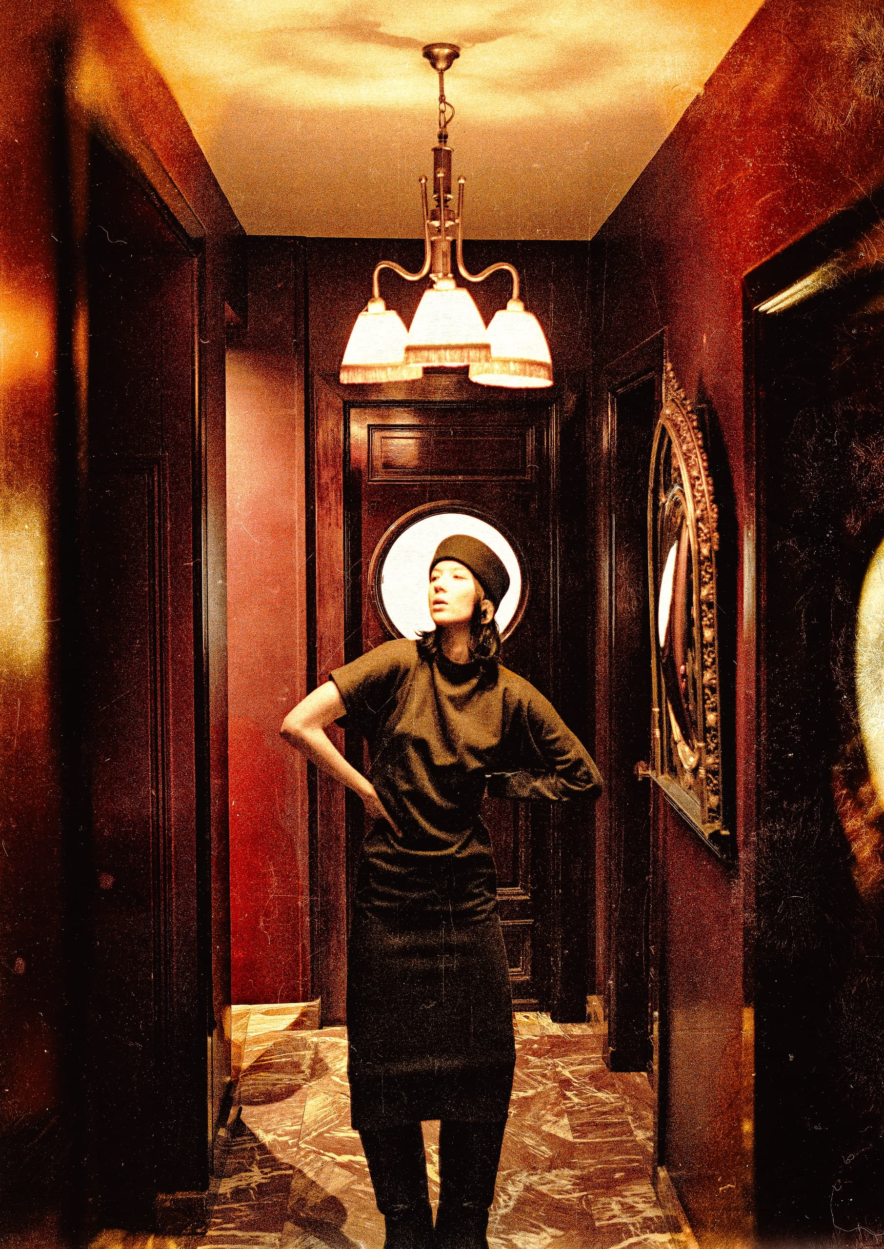 Mysterious woman in dimly lit hallway with vintage decor and warm lighting.