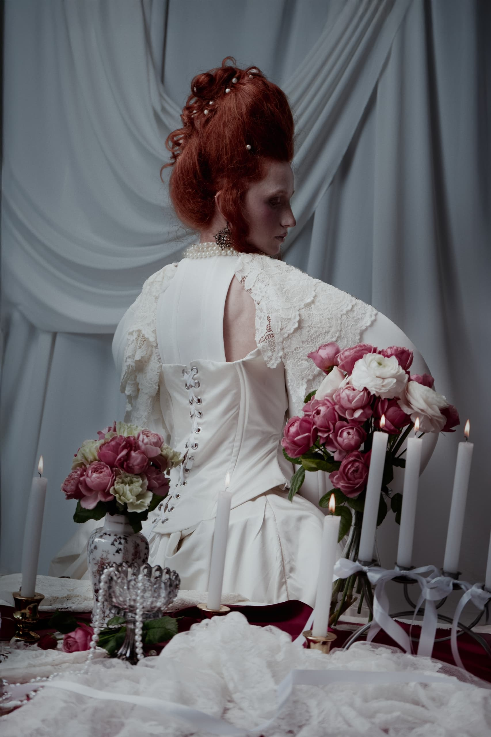 Elegant woman in vintage attire with roses and candles in a regal setting.
