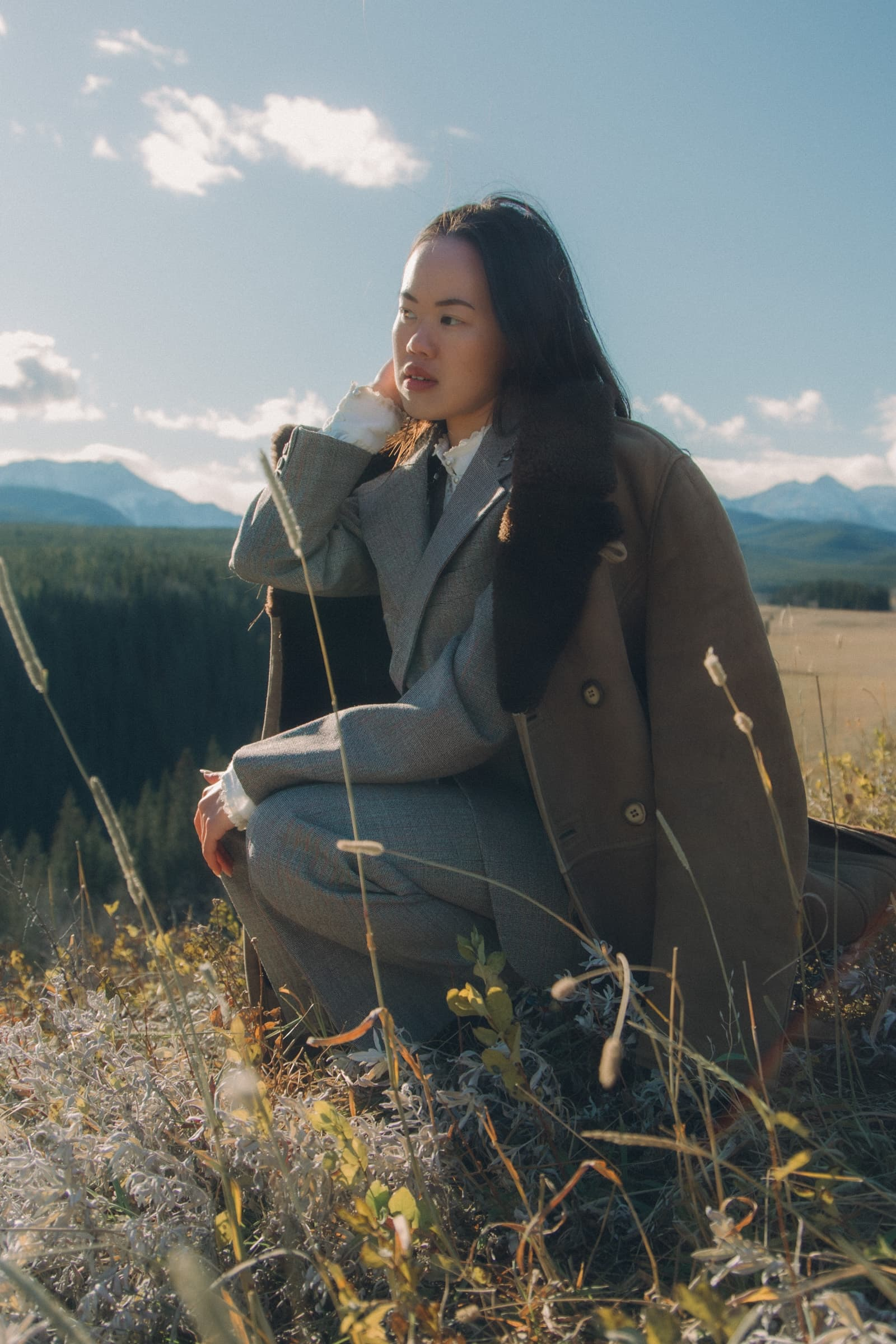Person in a suit sitting outdoors, scenic mountain view in the background.