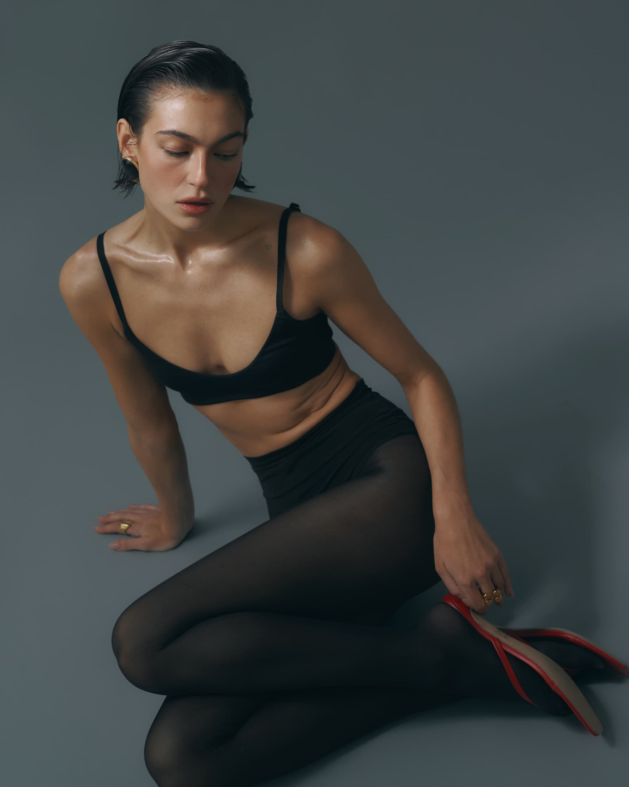 Woman in black attire sits gracefully with high heels, exuding elegance.