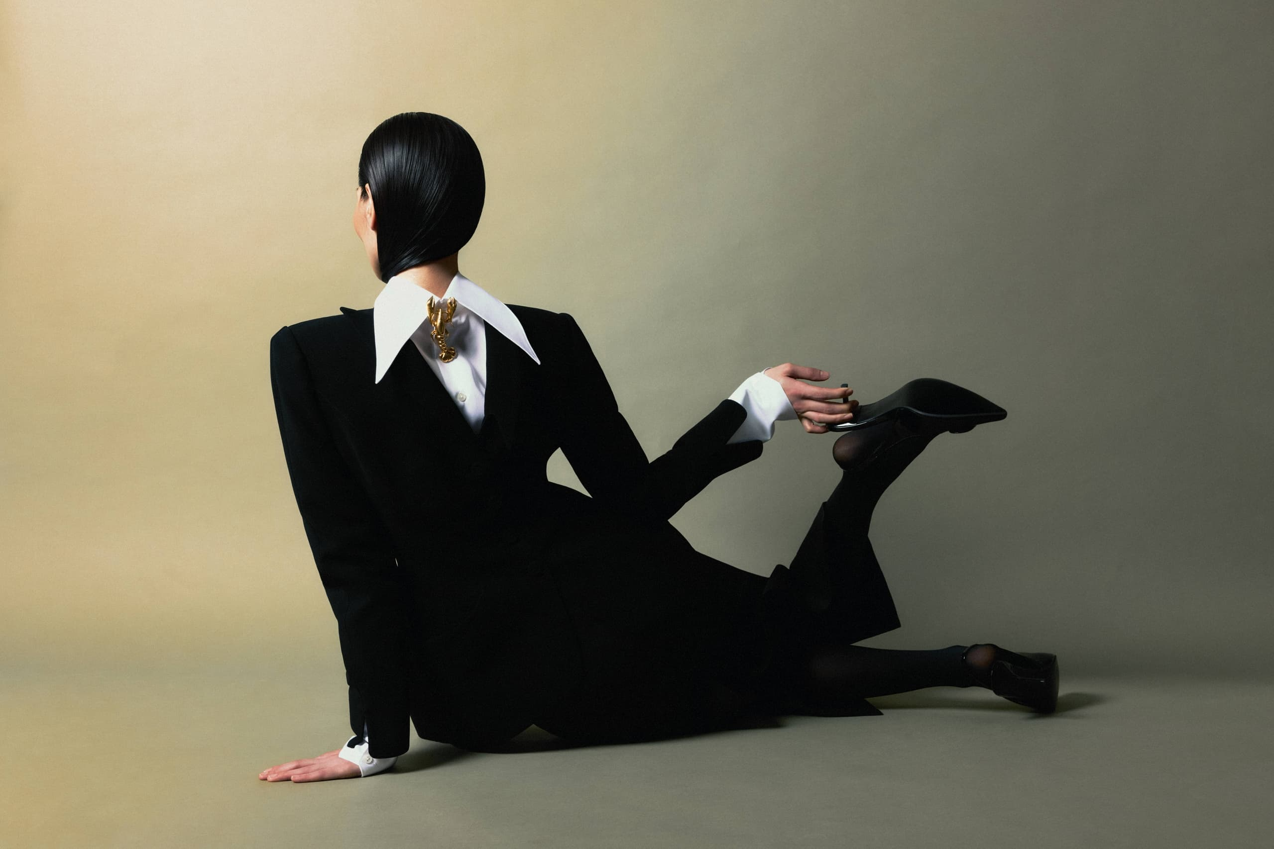 Fashionable person posing in a stylish suit with sleek hair, minimalist background.