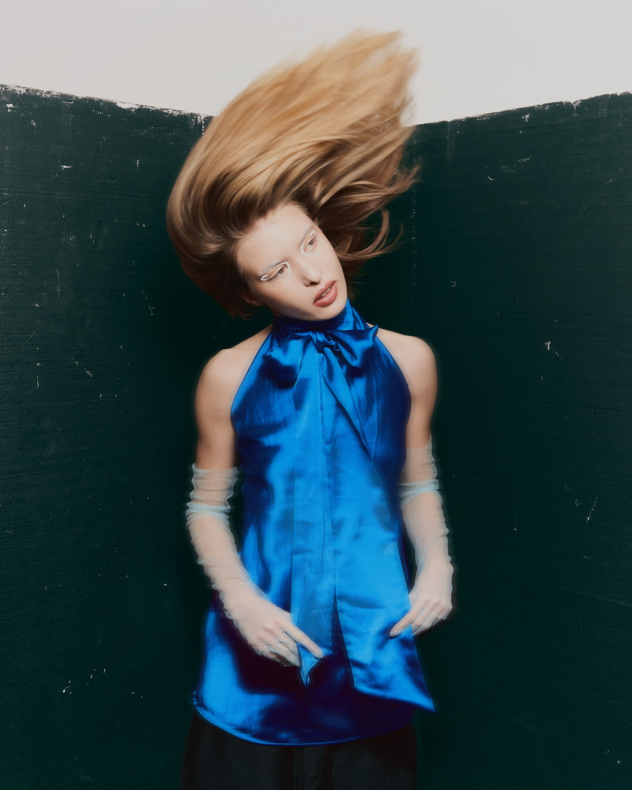 Model in vibrant blue top with dynamic hair motion against dark green background.