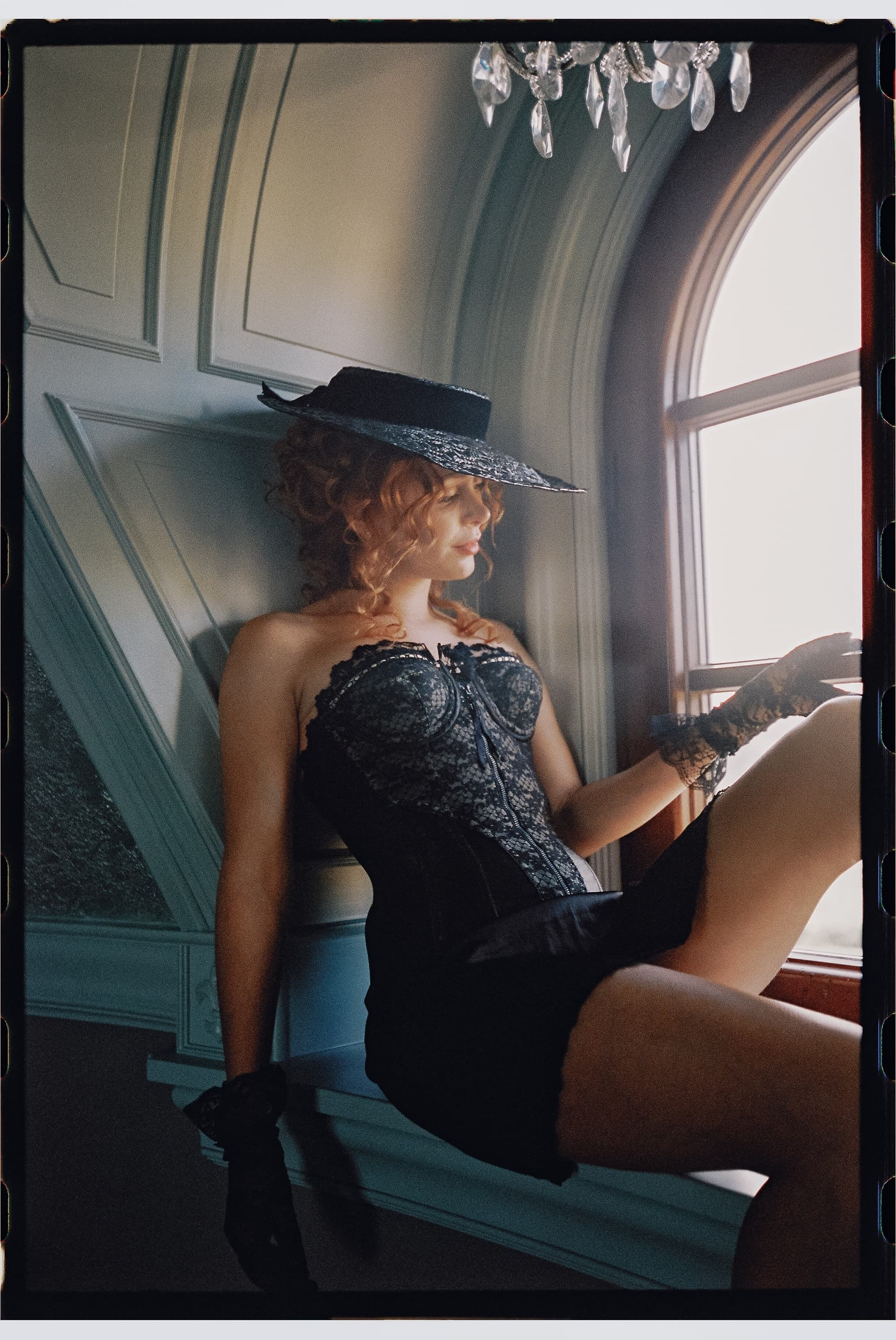 Woman in vintage attire sitting by an arched window.