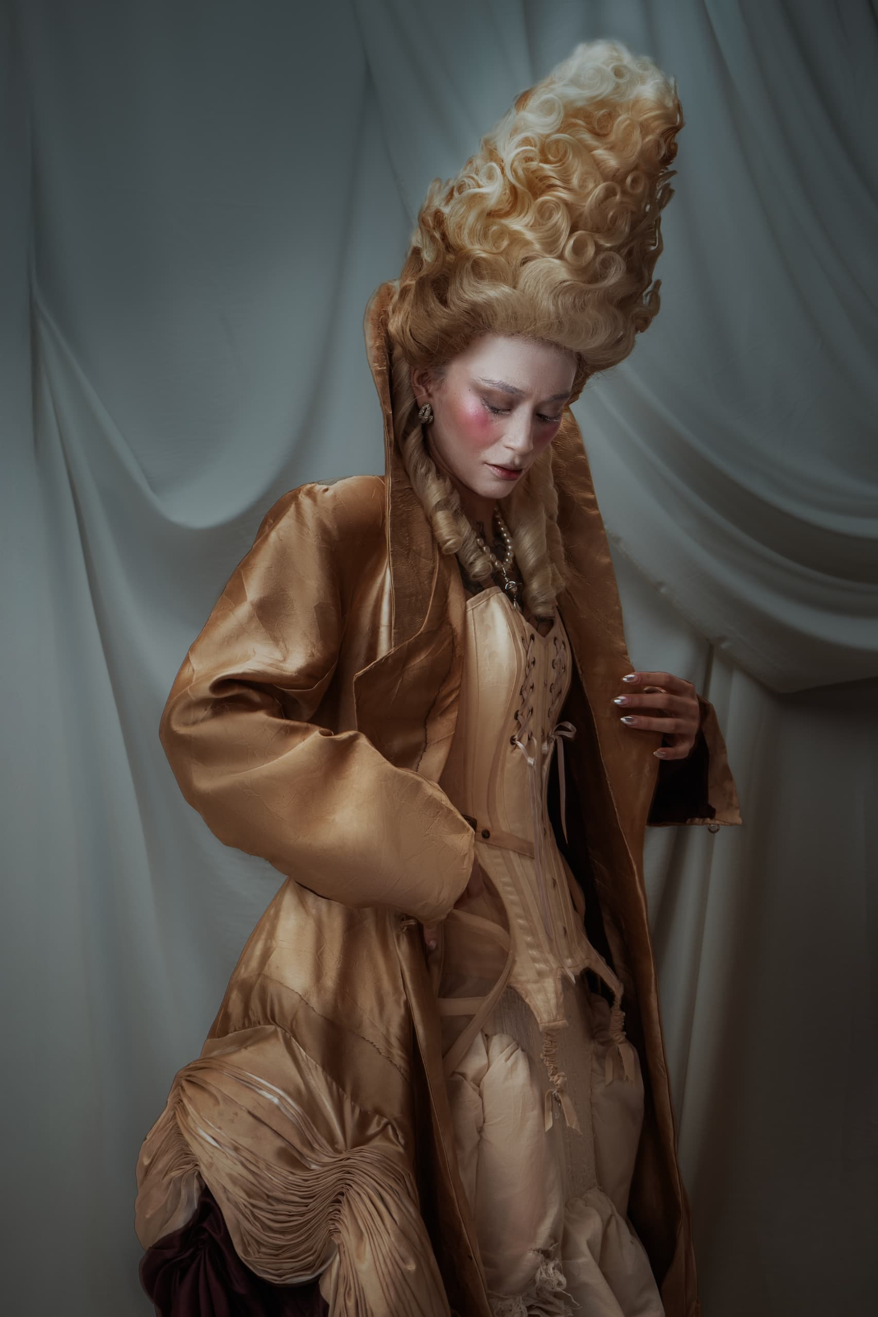 Elegant woman in elaborate Rococo-style gown and hairstyle against soft drapery backdrop.