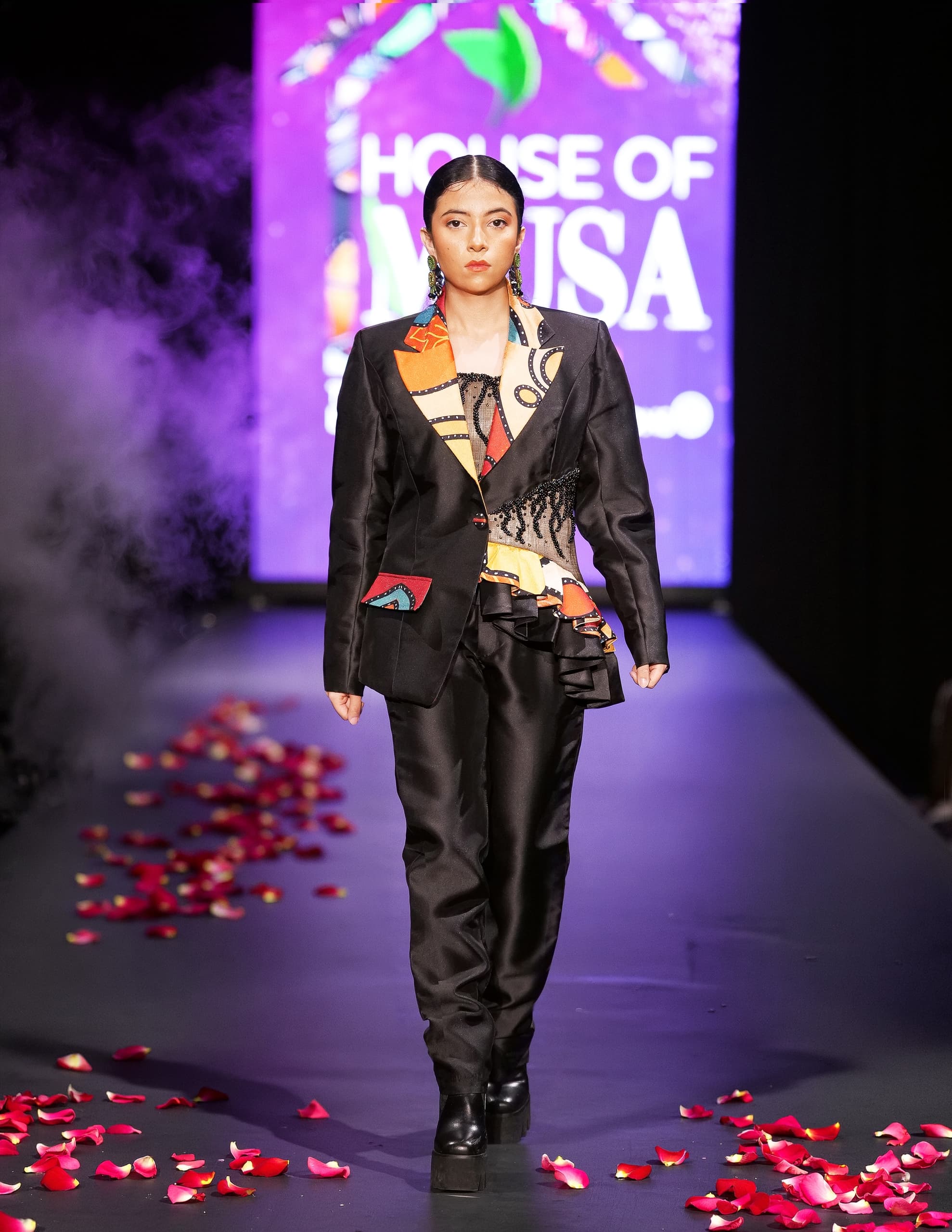 Model in vibrant outfit on runway with petals, House of Musa backdrop.