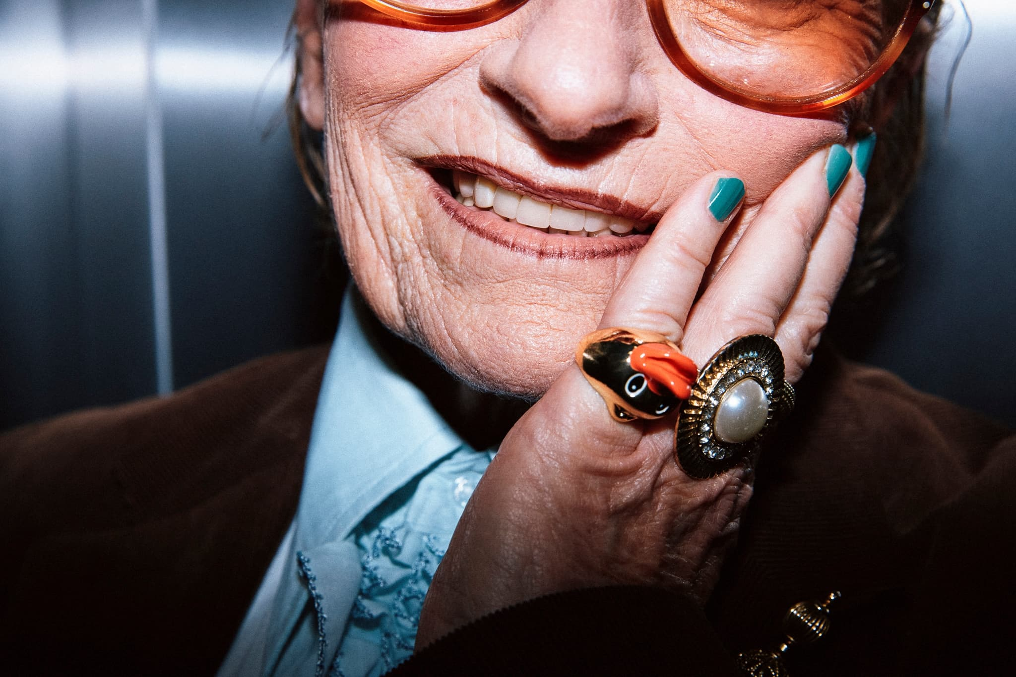 Smiling person with colorful nail polish and unique rings, wearing large glasses.