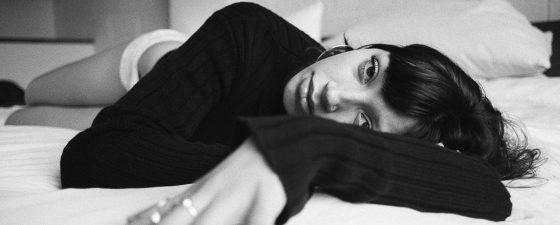 Black and white photo of a person resting on a bed, wearing a dark sweater.
