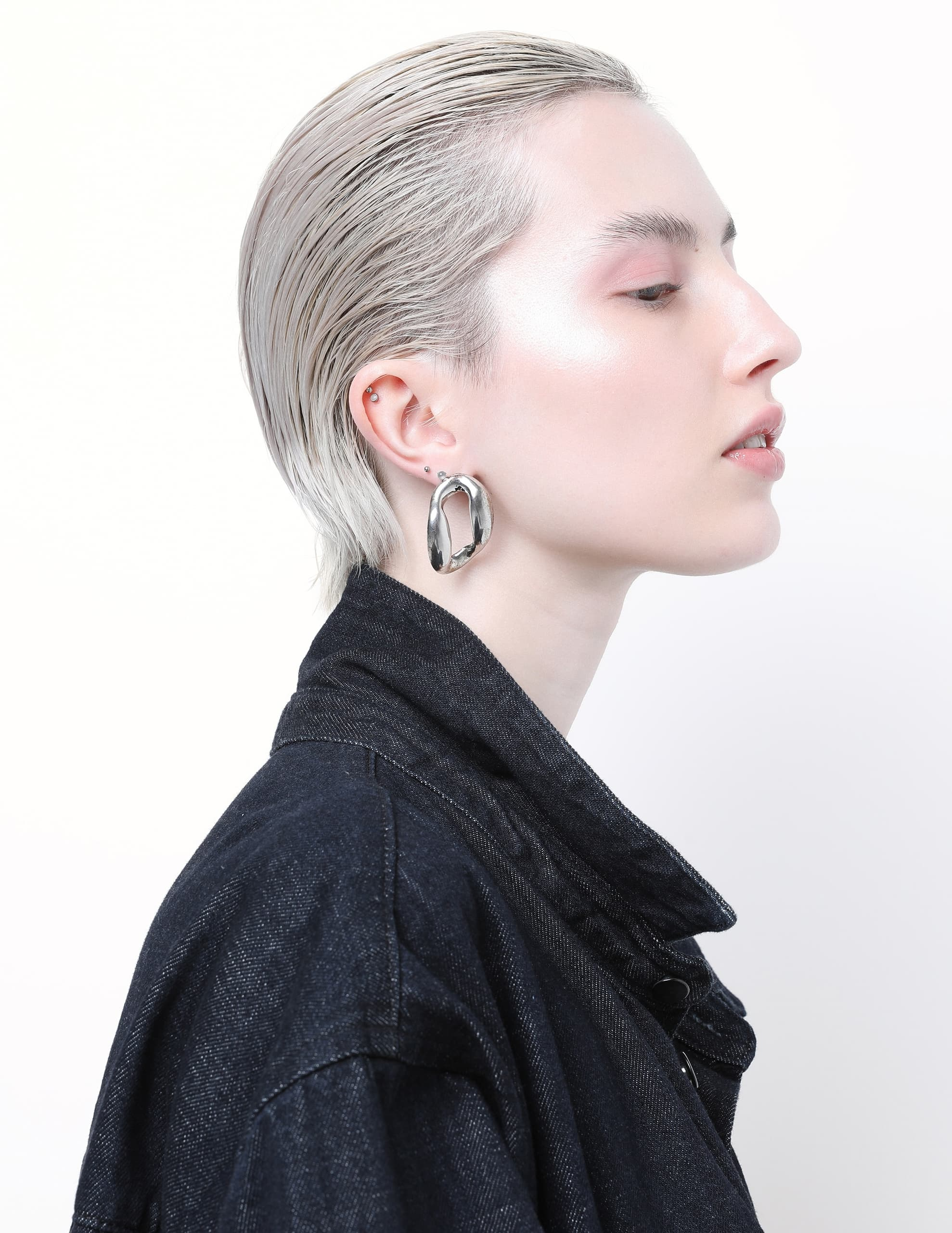 Profile of person in denim jacket with sleek hair and silver hoop earrings.