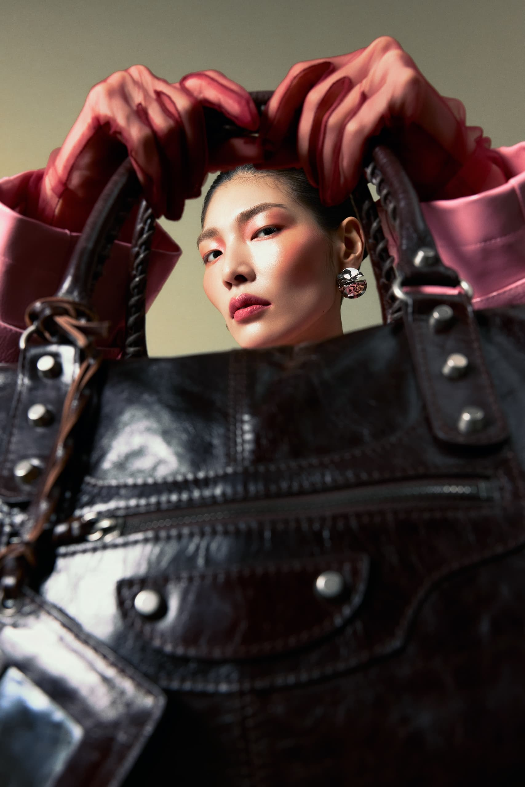 Close-up of woman holding a stylish leather handbag with pink outfit gloves.
