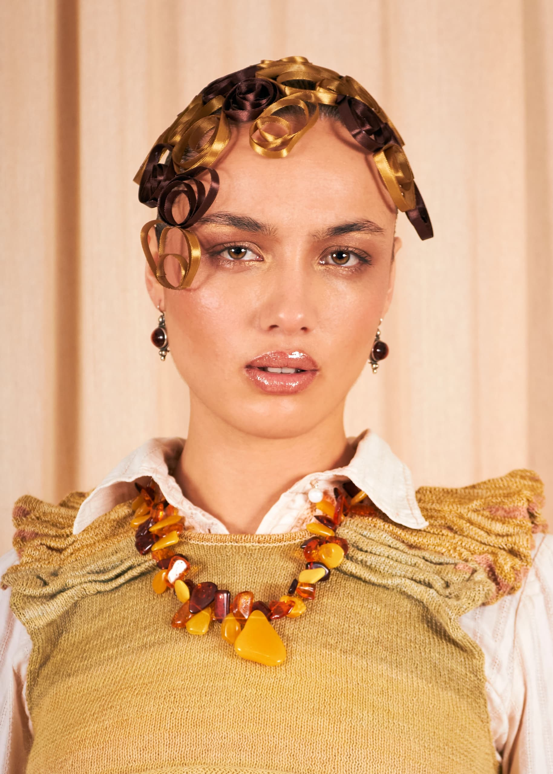 Woman with curly ribbon hair, beaded amber necklace, and a stylish textured top.