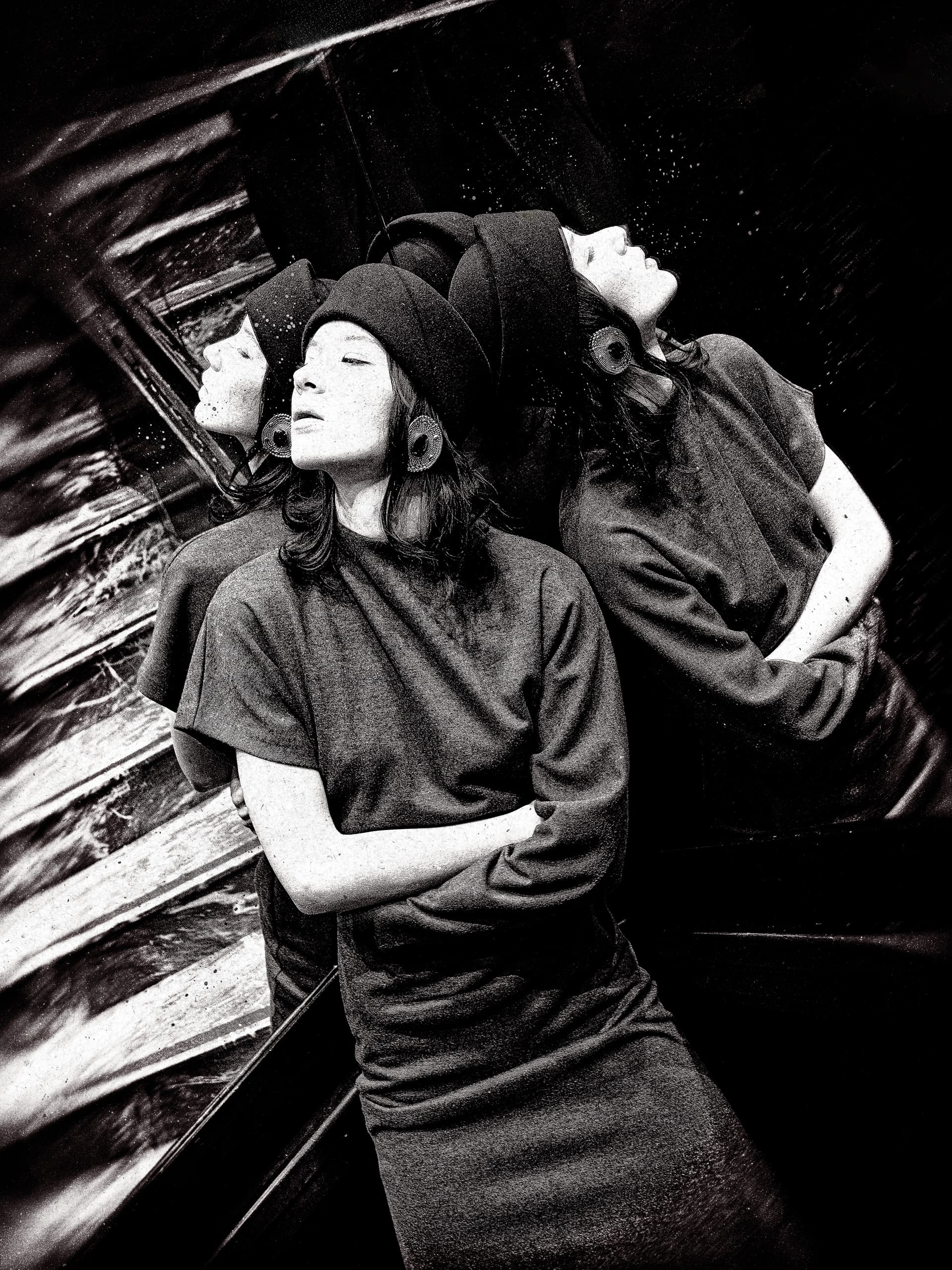 Vintage-style portrait of a woman in front of mirrors, wearing a hat and earrings.