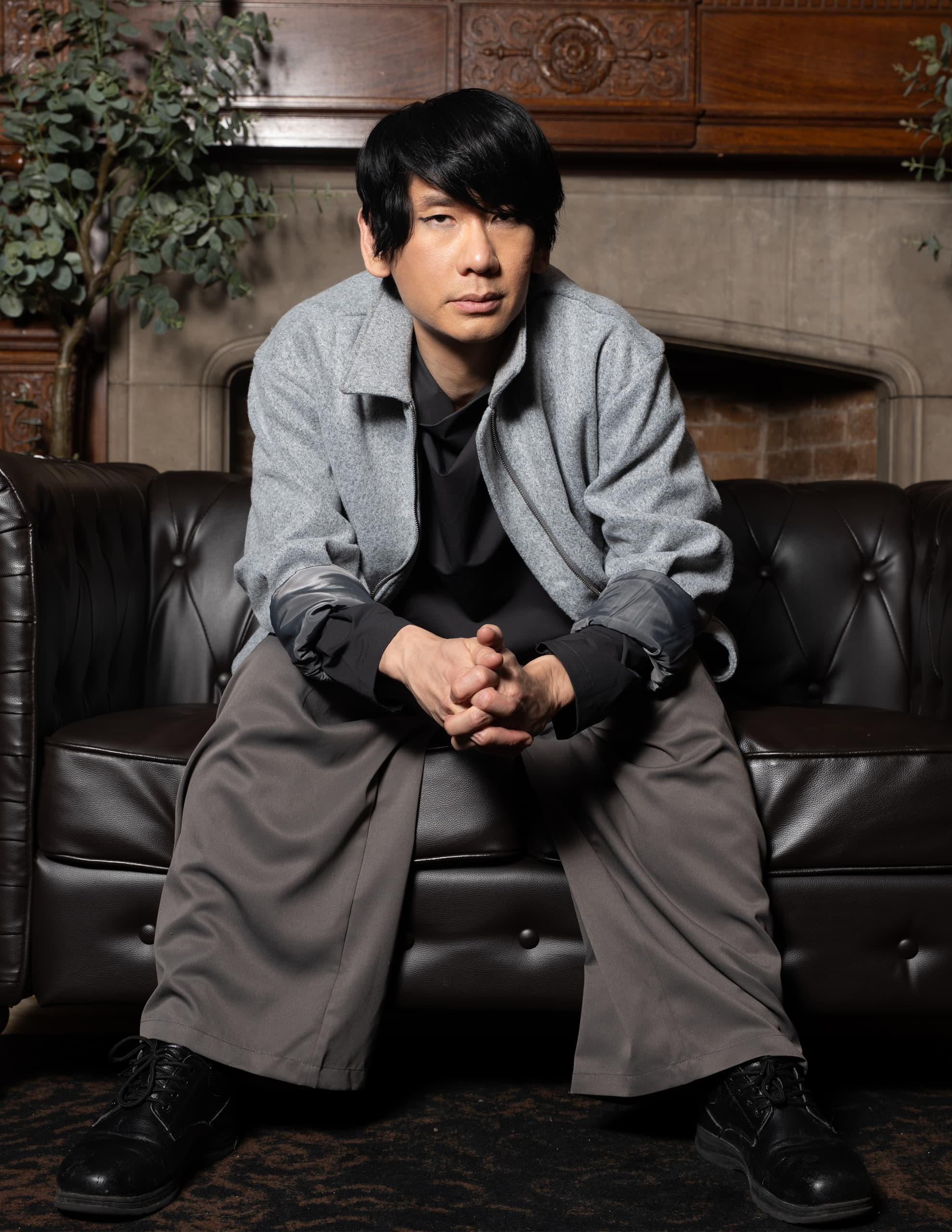 Man in gray jacket seated on a leather sofa in a cozy, vintage setting.