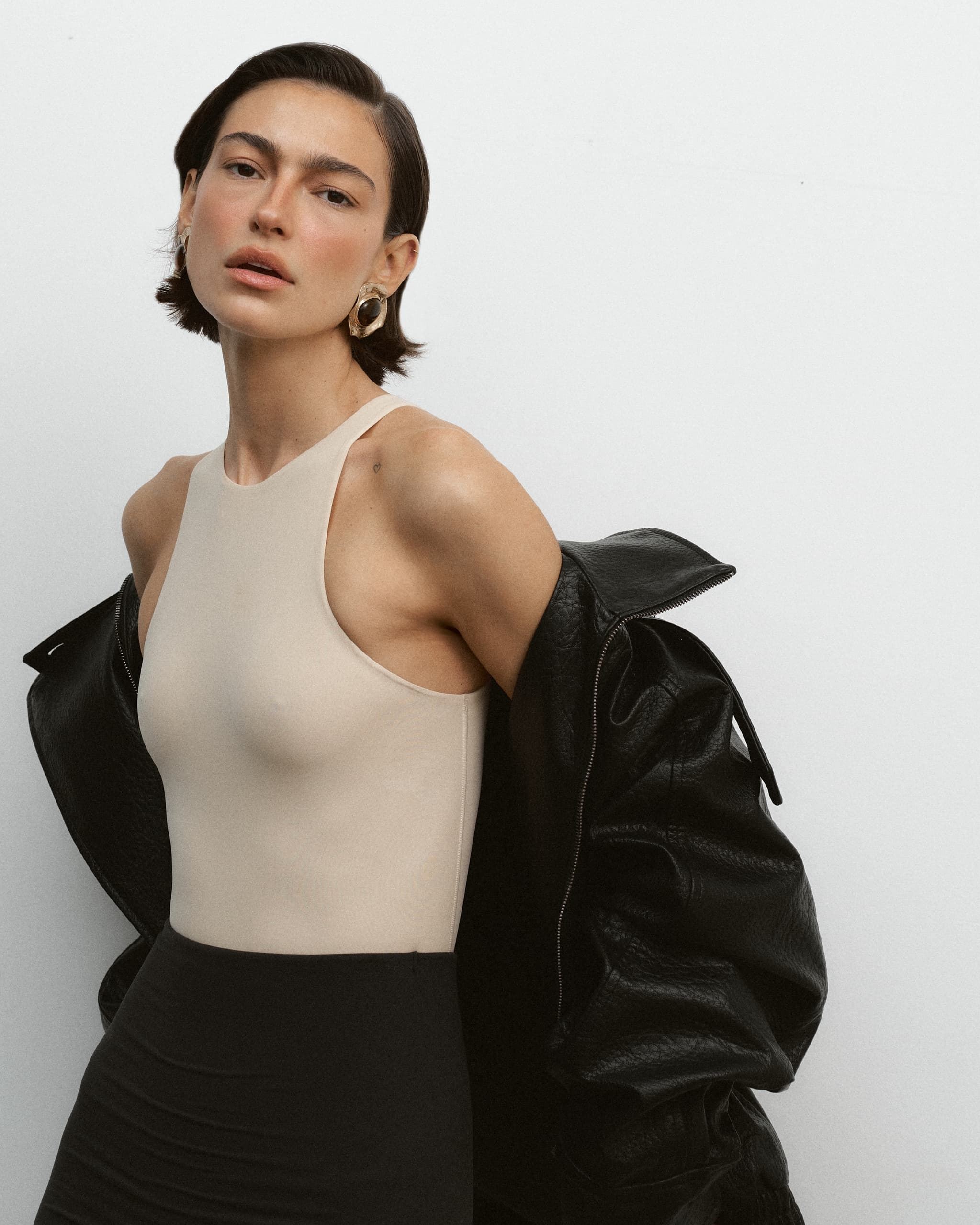 Fashionable woman in neutral top and leather jacket, minimalist style.