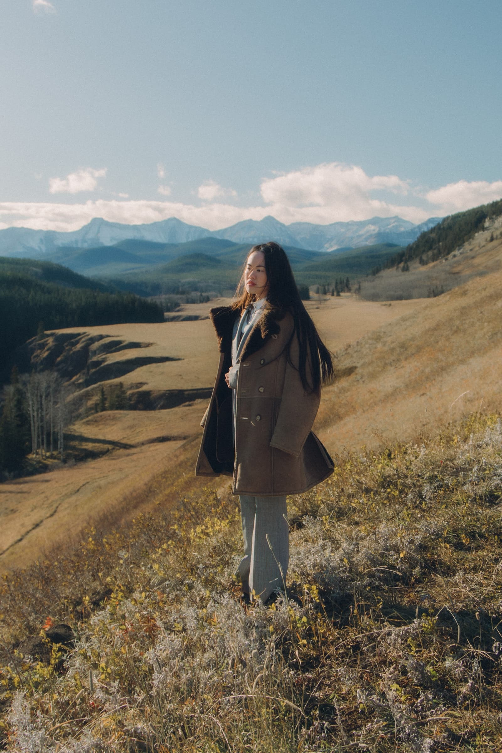 Person in a brown coat enjoying a scenic mountain view under a clear sky.
