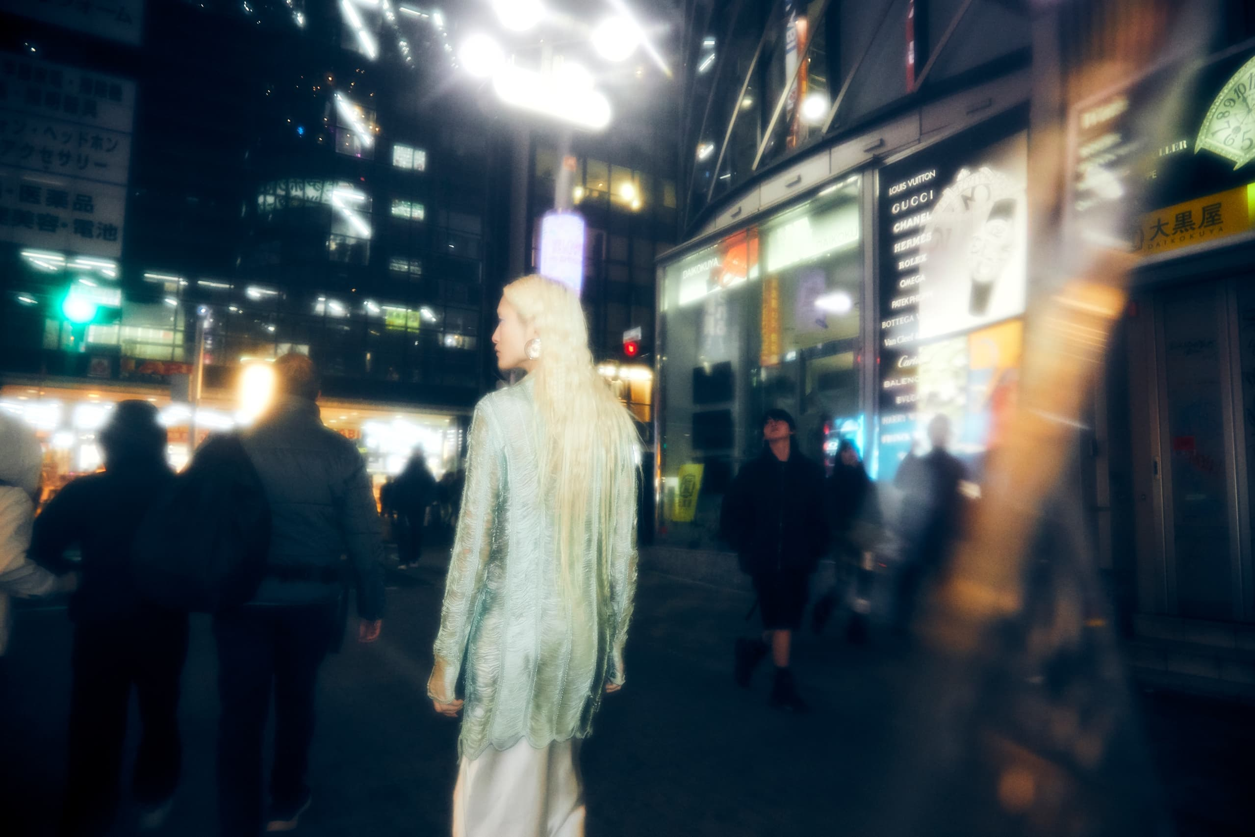 Fashionable woman in a vibrant city street at night with blurred neon lights.
