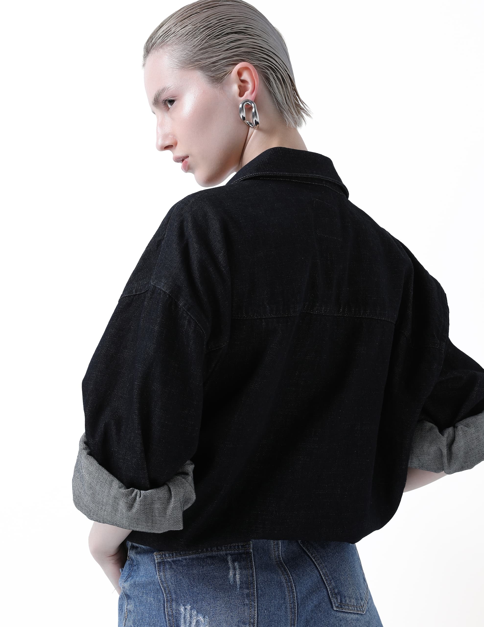 Fashionable person in denim and black top, showcasing modern earrings.