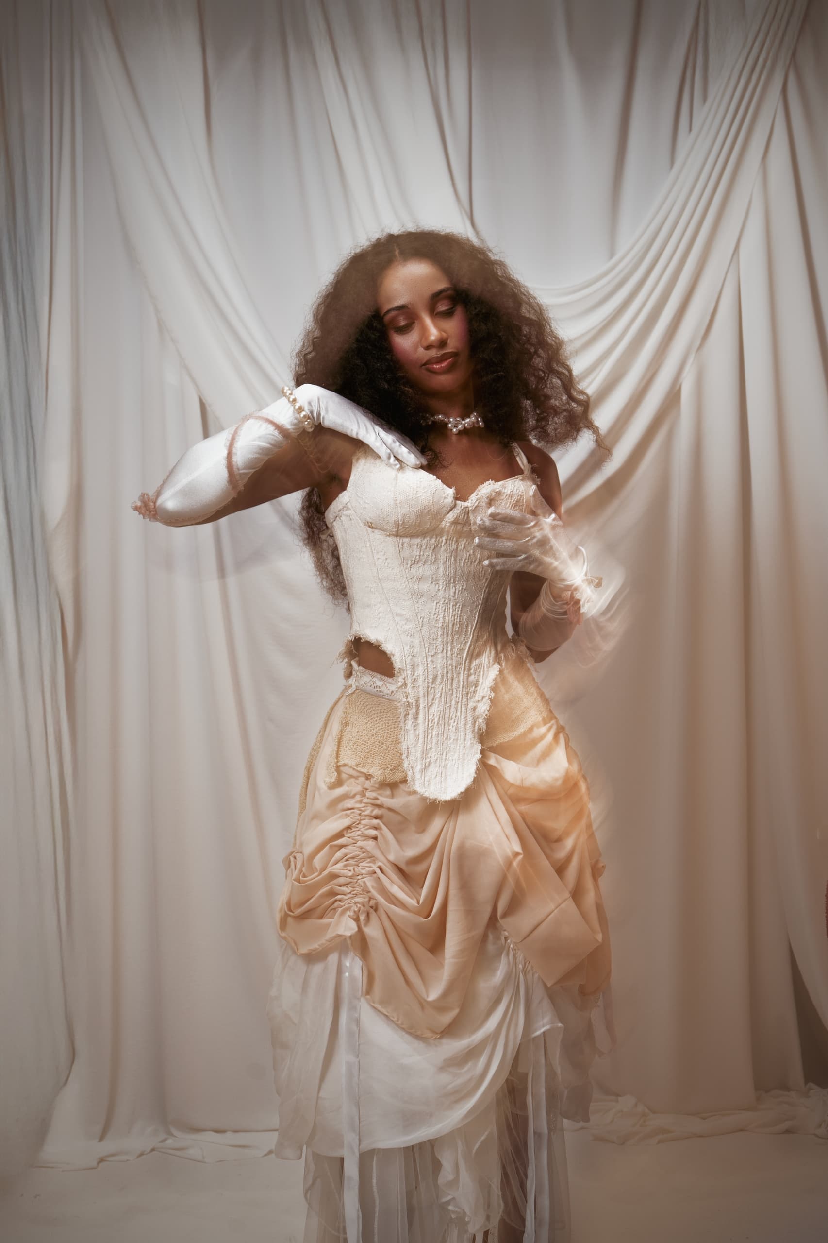 Woman in elegant vintage dress posing in front of flowing white drapery.