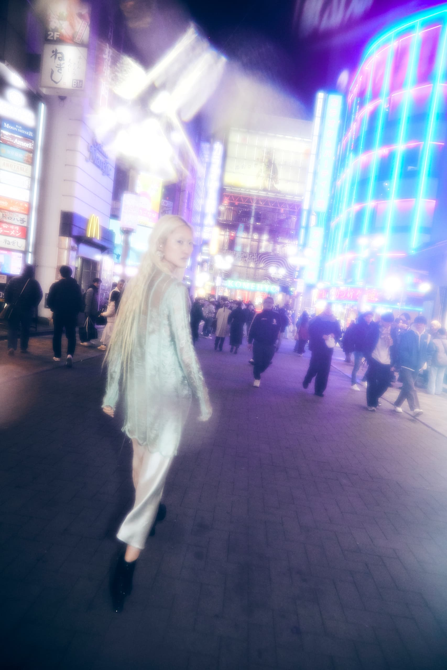 Person walking in bright, neon-lit city street, with a dreamlike atmosphere.