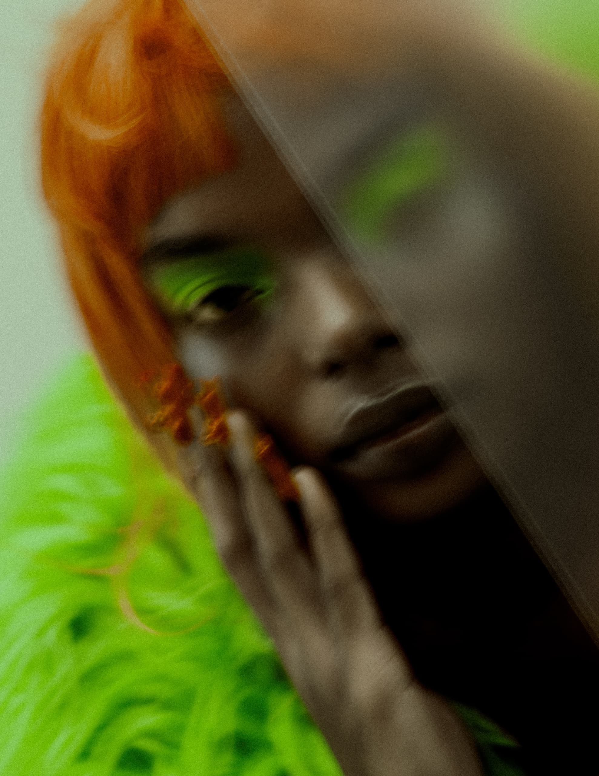 Vibrant portrait with bright orange hair and neon green accents, hand on face.