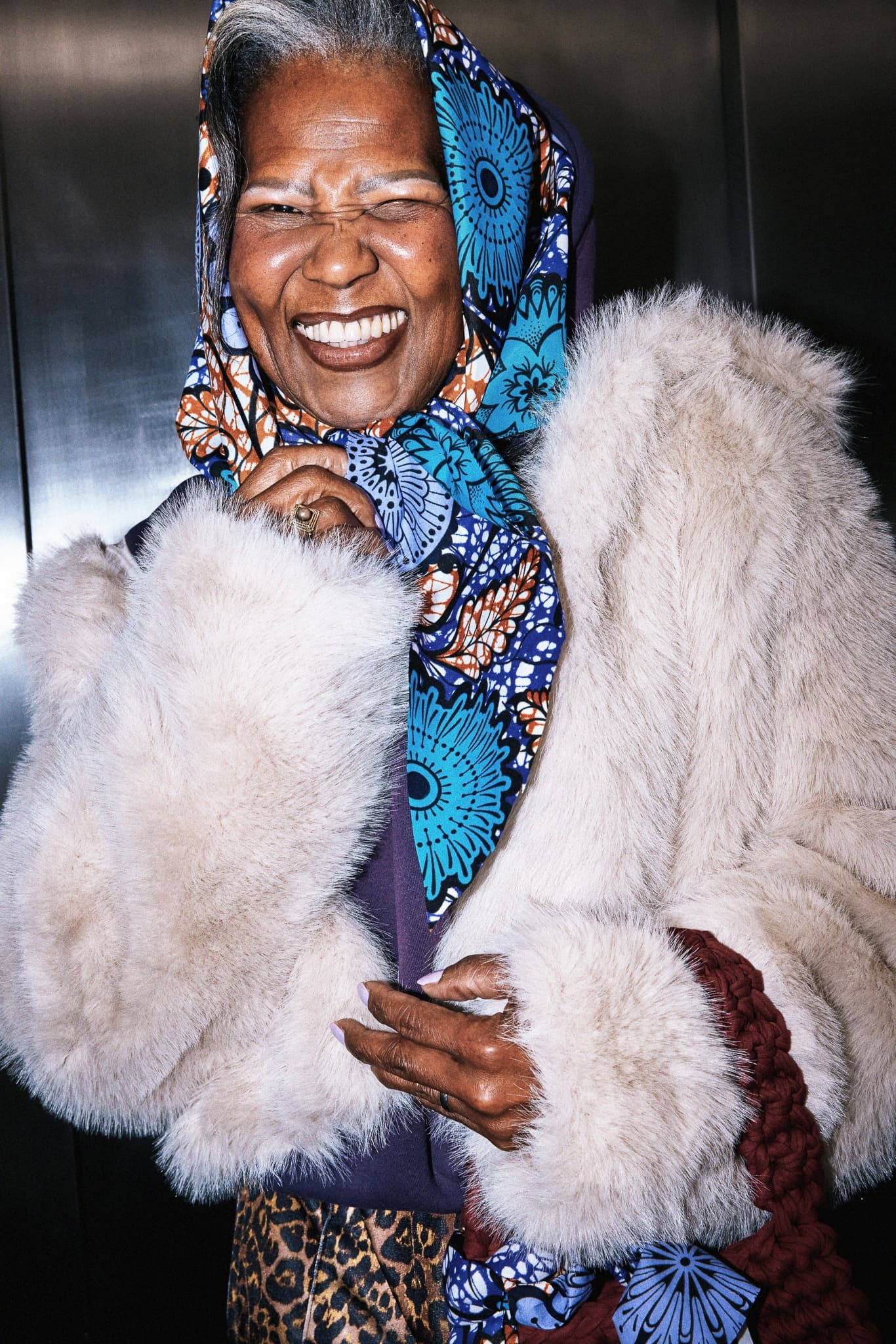 Smiling woman in colorful headscarf and fur coat, expressing joy and elegance.