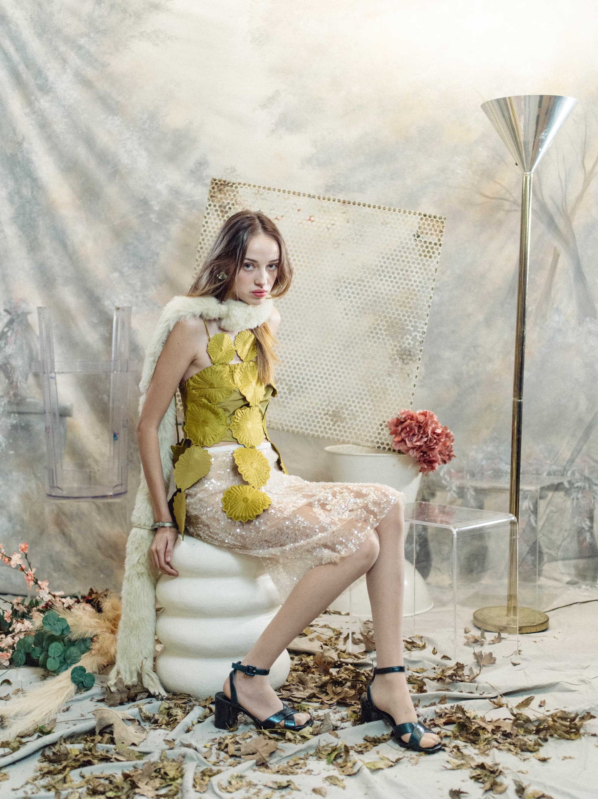 Stylish woman in unique outfit, seated in artful, nature-inspired setting.